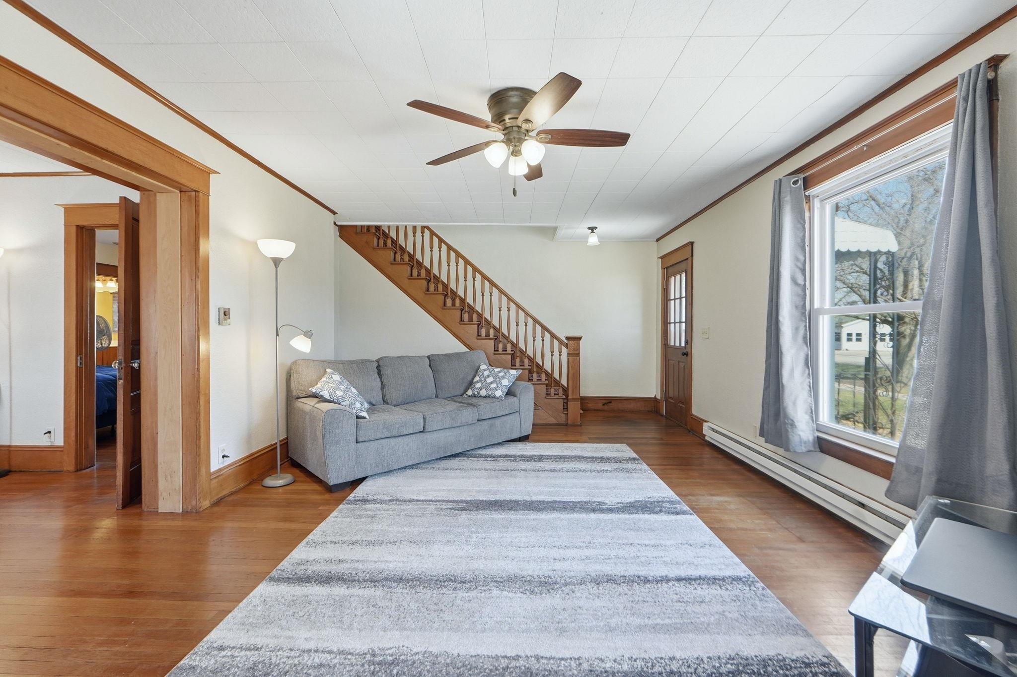 Living room with a baseboard radiator, ceiling fan, dark wood-style floors, and crown molding