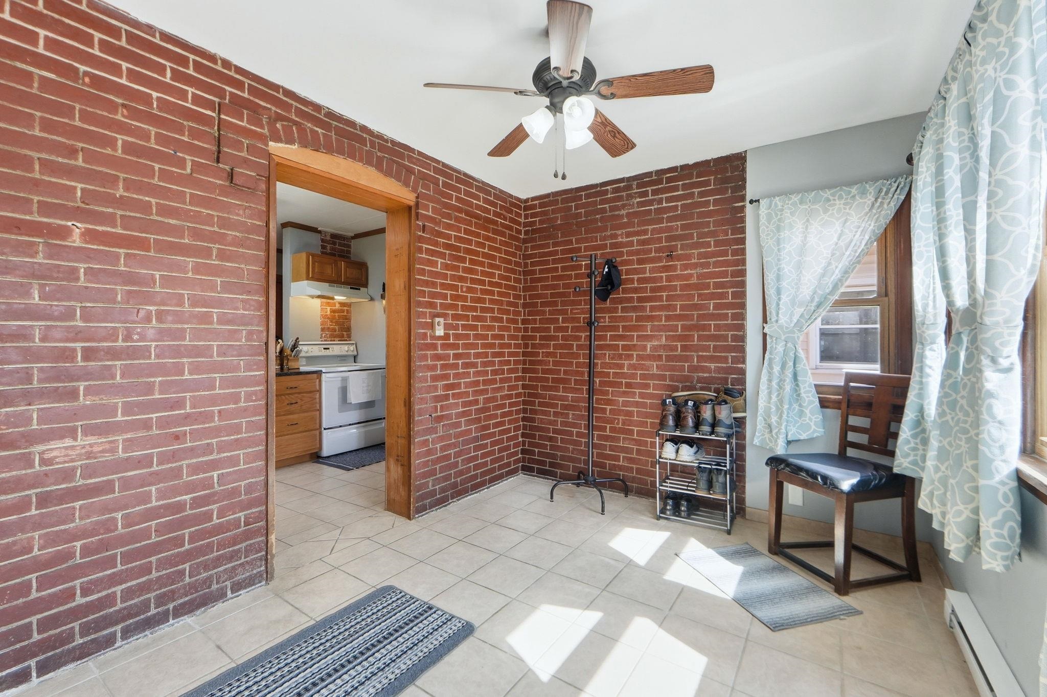 Living area with a baseboard heating unit, a ceiling fan, light tile patterned floors, and brick wall