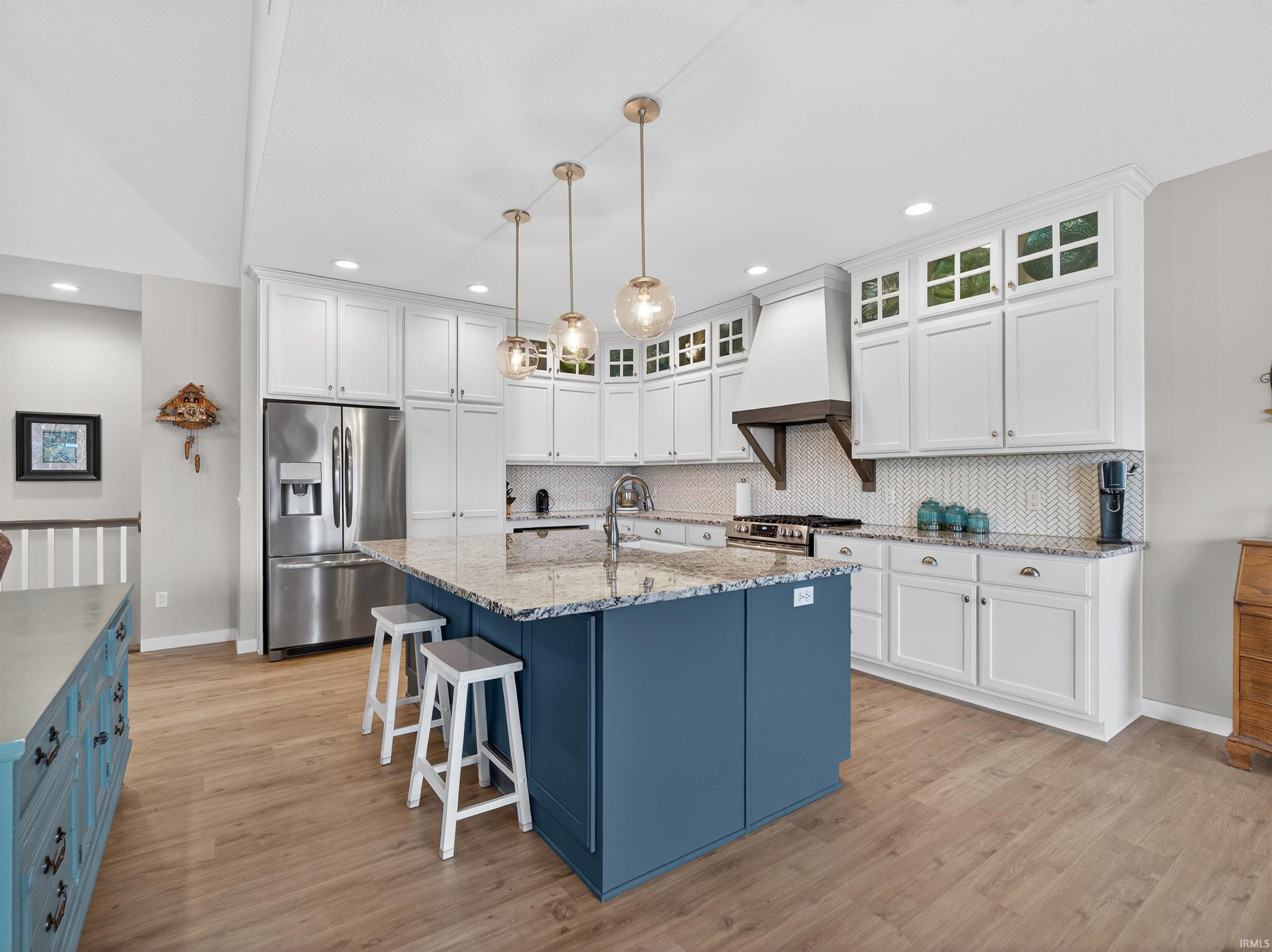 Two tone kitchen featuring dual tone cabinetry, tasteful backsplash, stainless steel appliances, an island with sink, and glass fronted cabinets