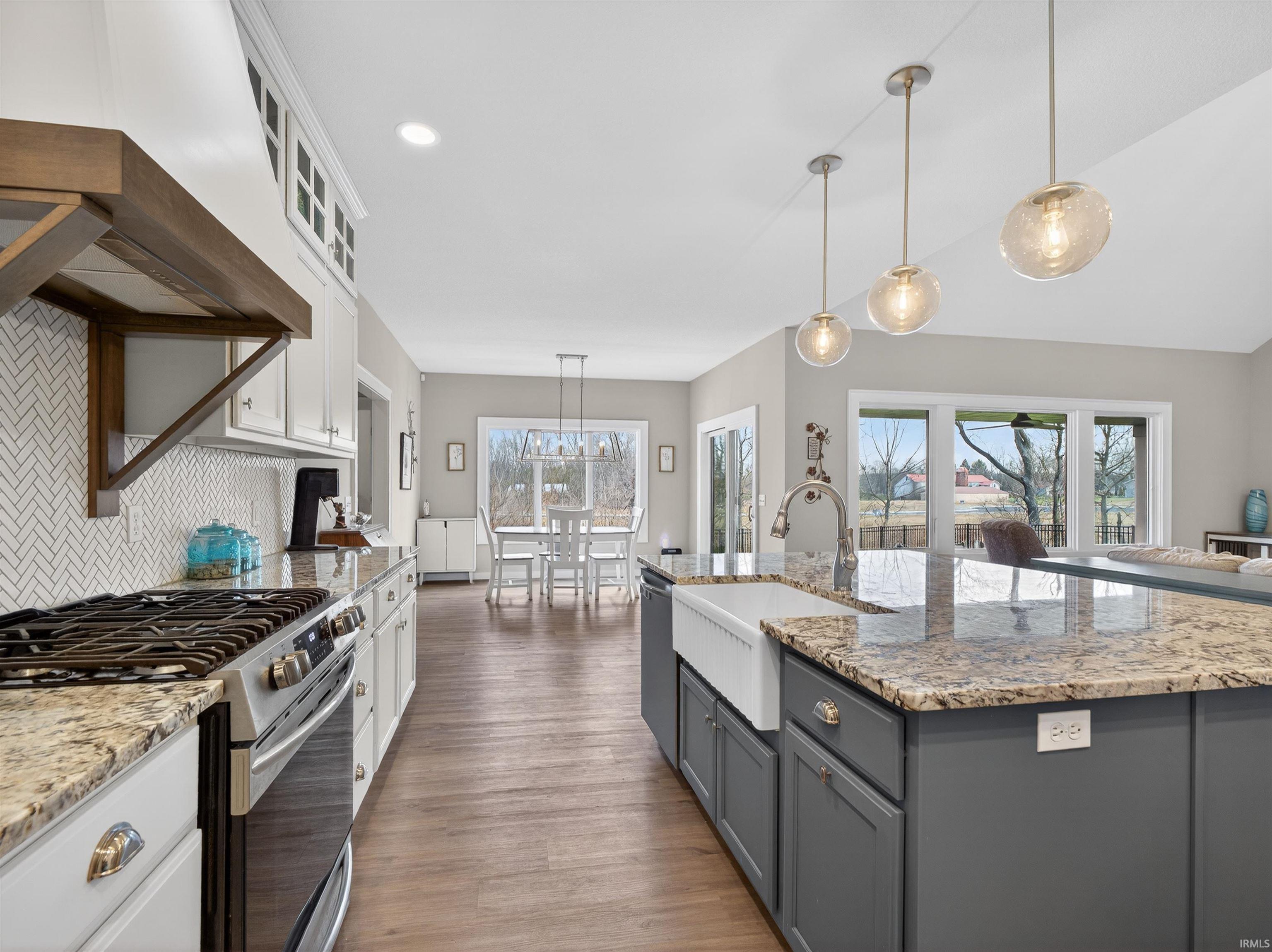 Kitchen with dual tone cabinets, stainless steel gas range oven, light stone counters, decorative light fixtures, and dark wood-type flooring