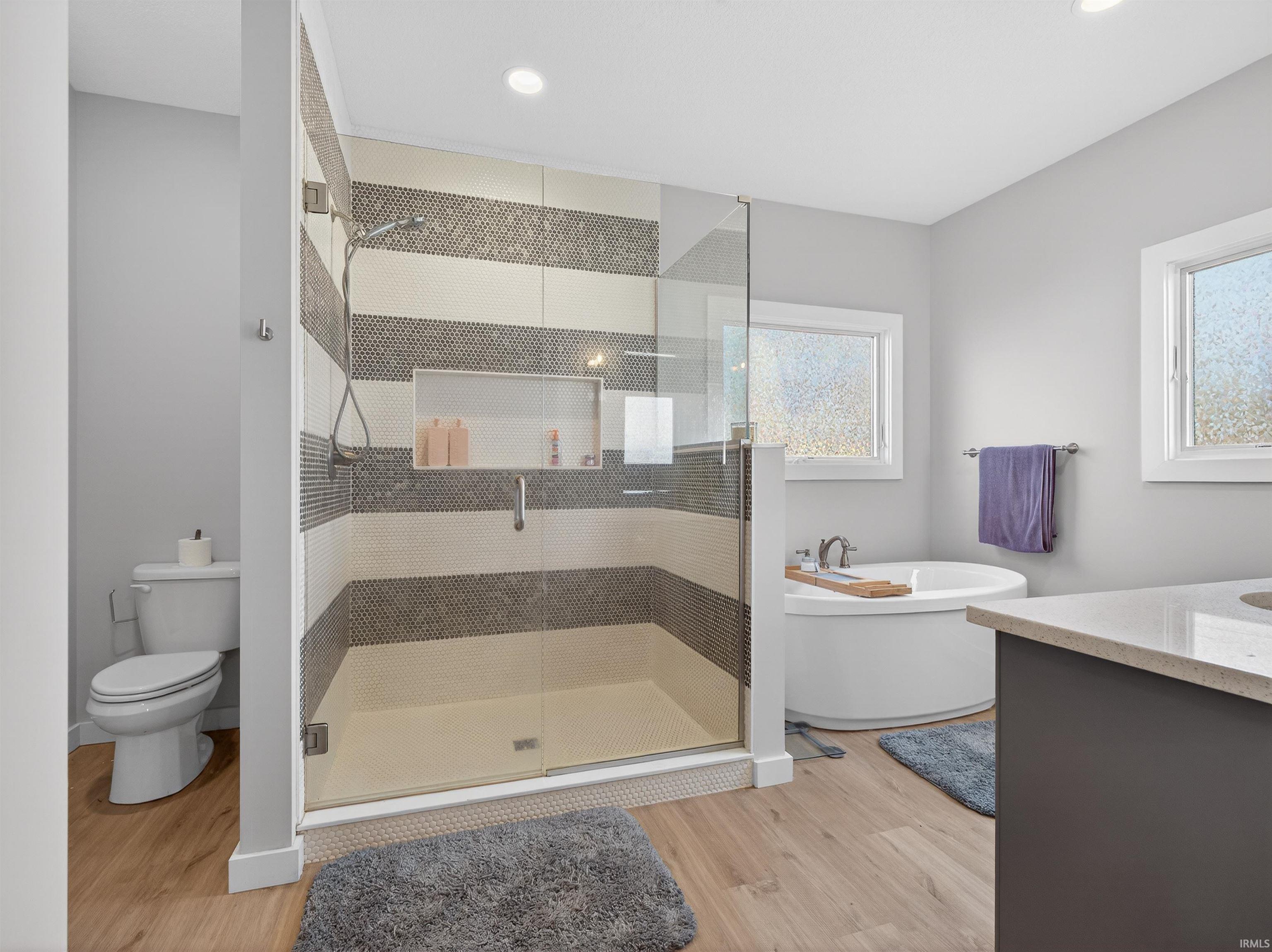 Bathroom featuring vanity, a soaking tub, light wood-style floors, a stall shower, and recessed lighting