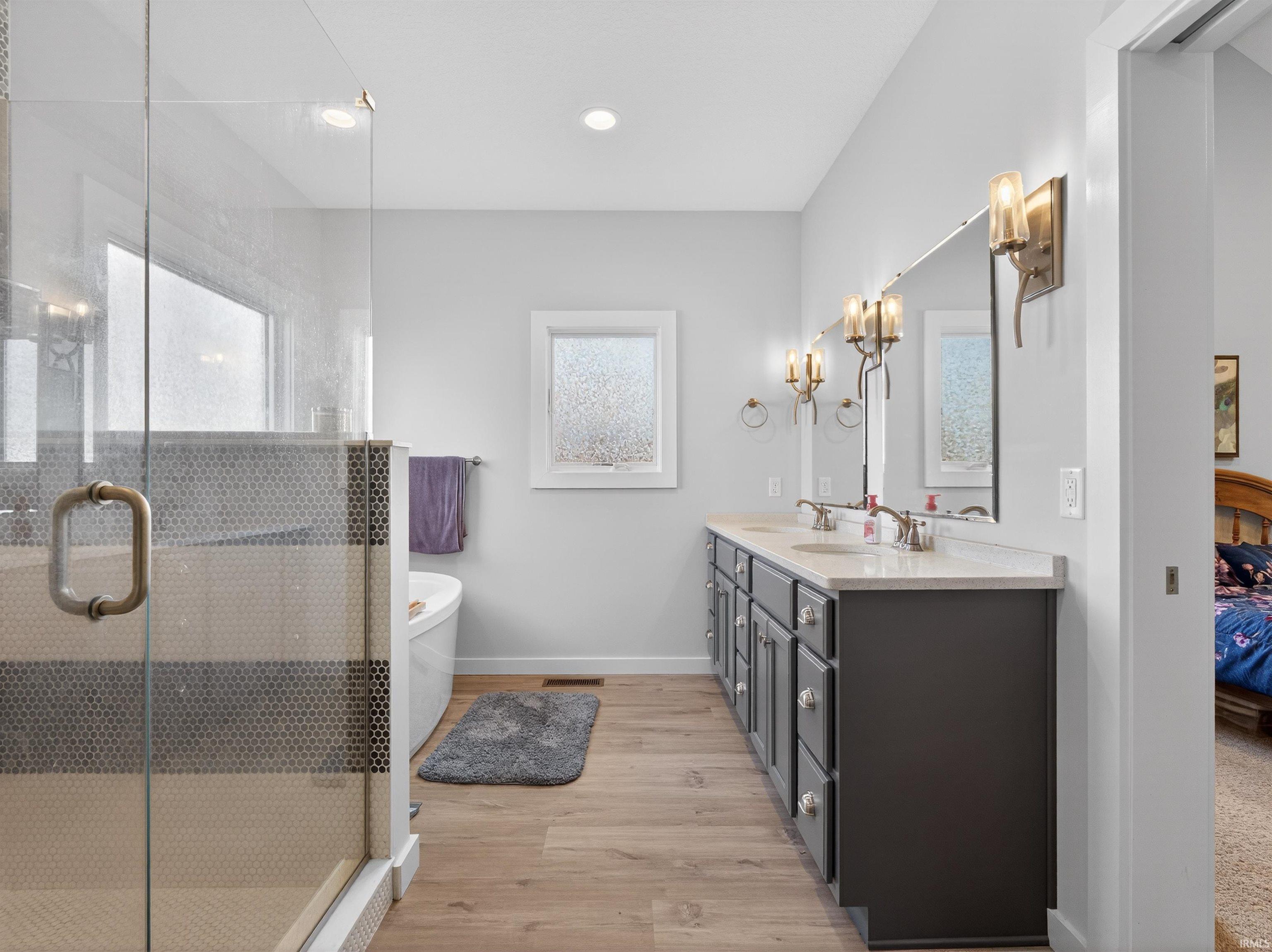 Bathroom with double vanity, light wood-style flooring, a stall shower, a freestanding tub, and ensuite bathroom