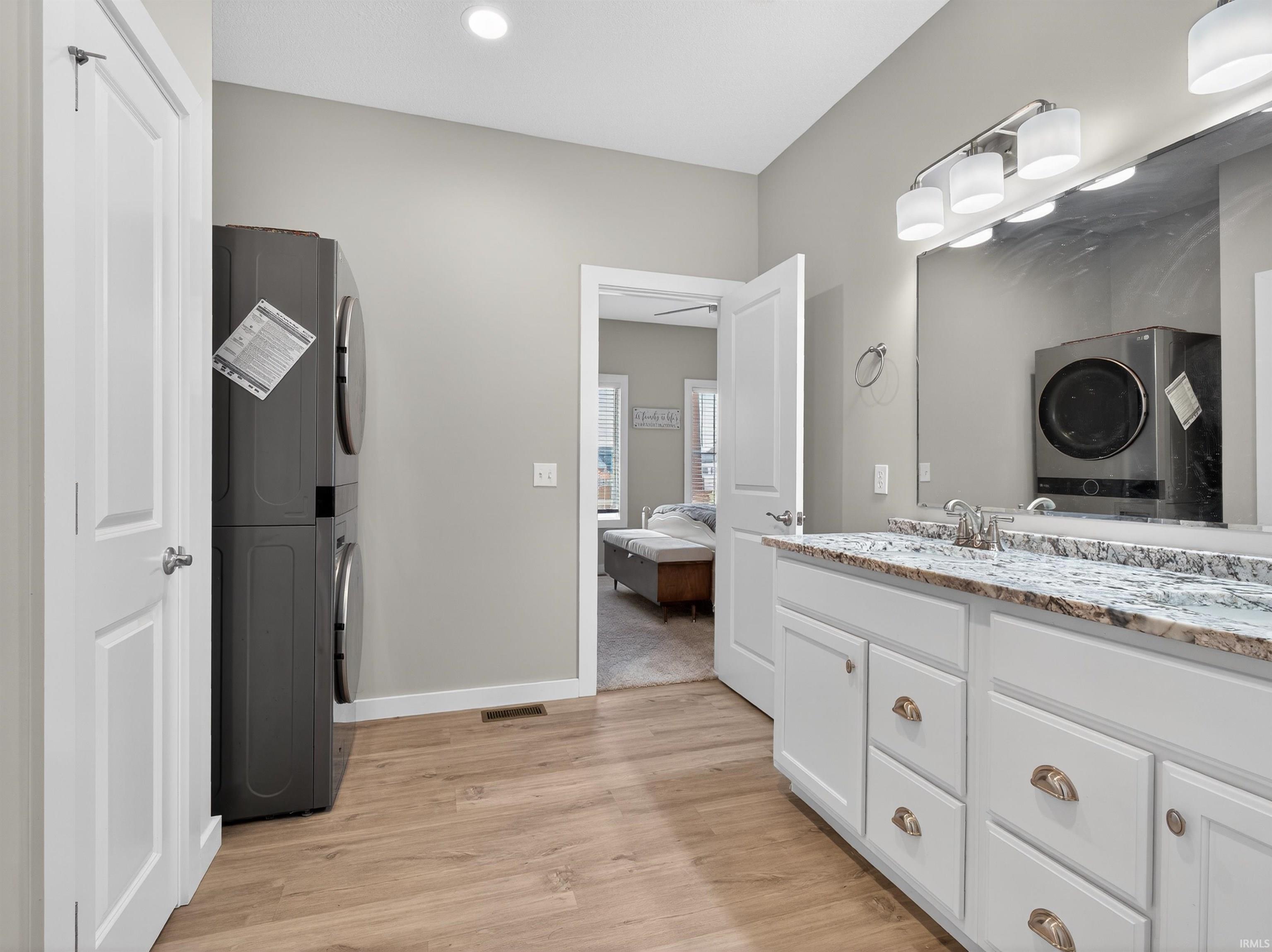 Ensuite bathroom with stacked washer and dryer, vanity, light wood-style floors, and recessed lighting