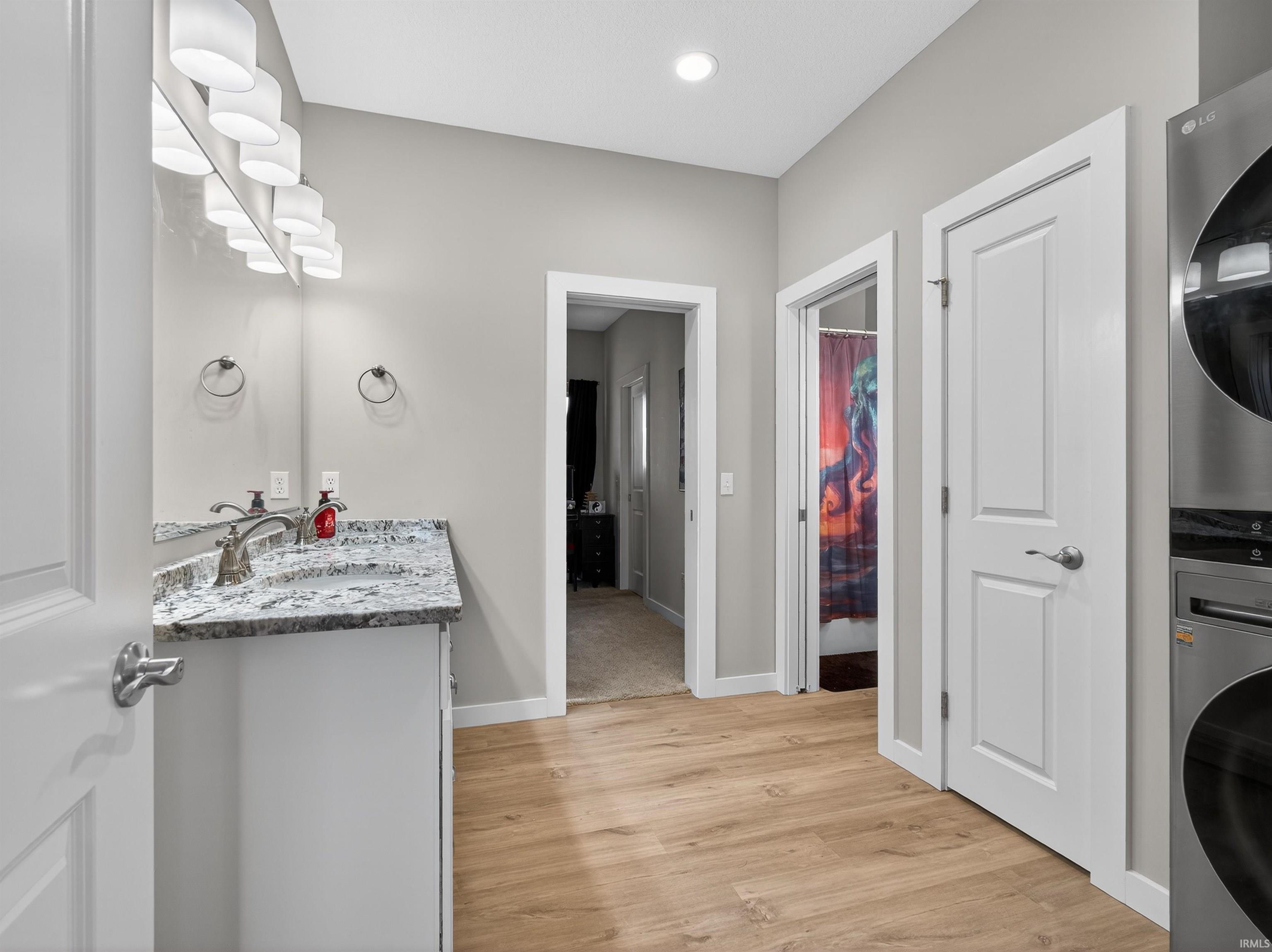 Bathroom featuring vanity, light wood-style flooring, stacked washer / drying machine, curtained shower, and recessed lighting