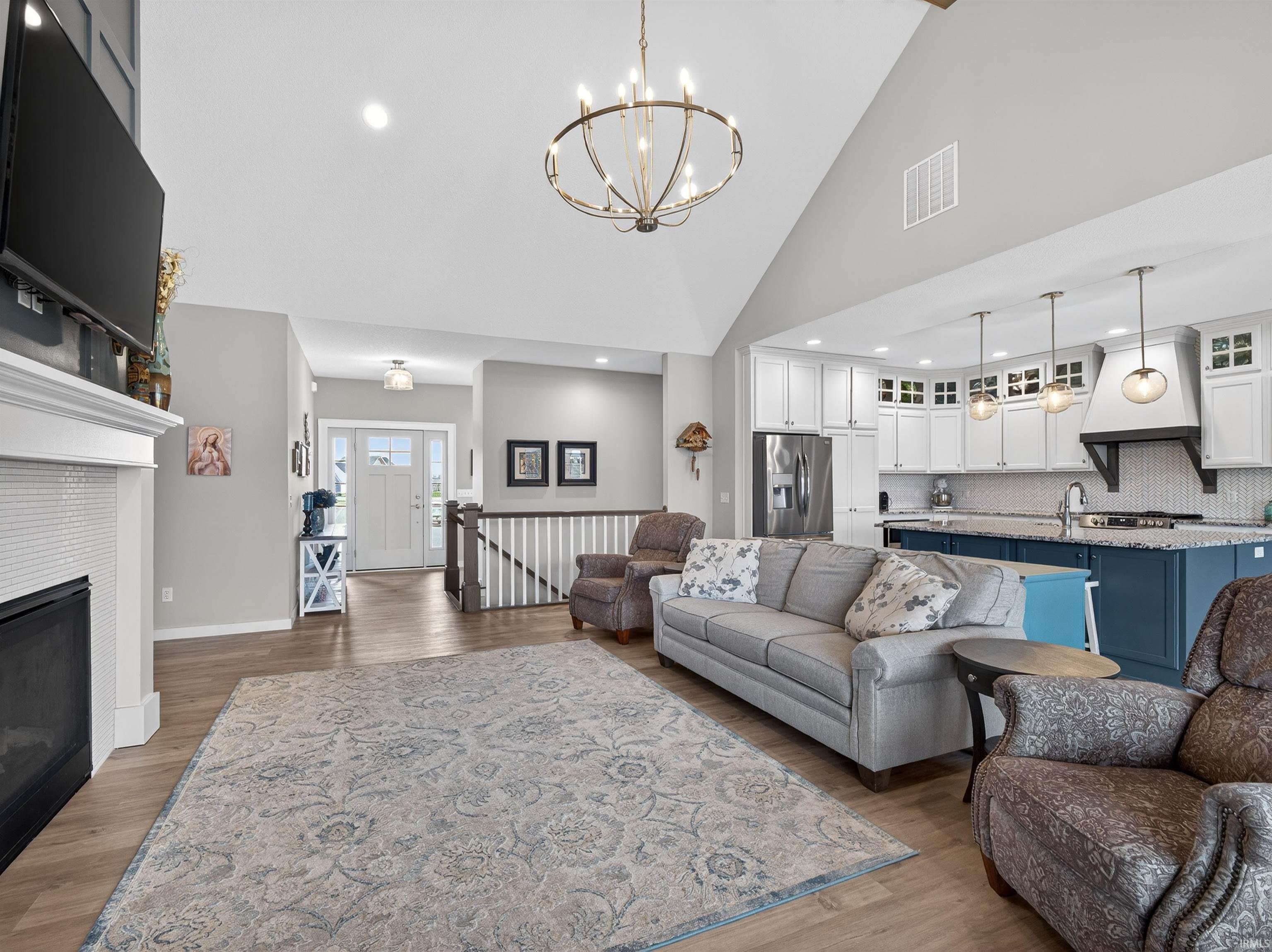 Living room with light wood finished floors, suspended lighting, a tiled fireplace, and vaulted ceiling
