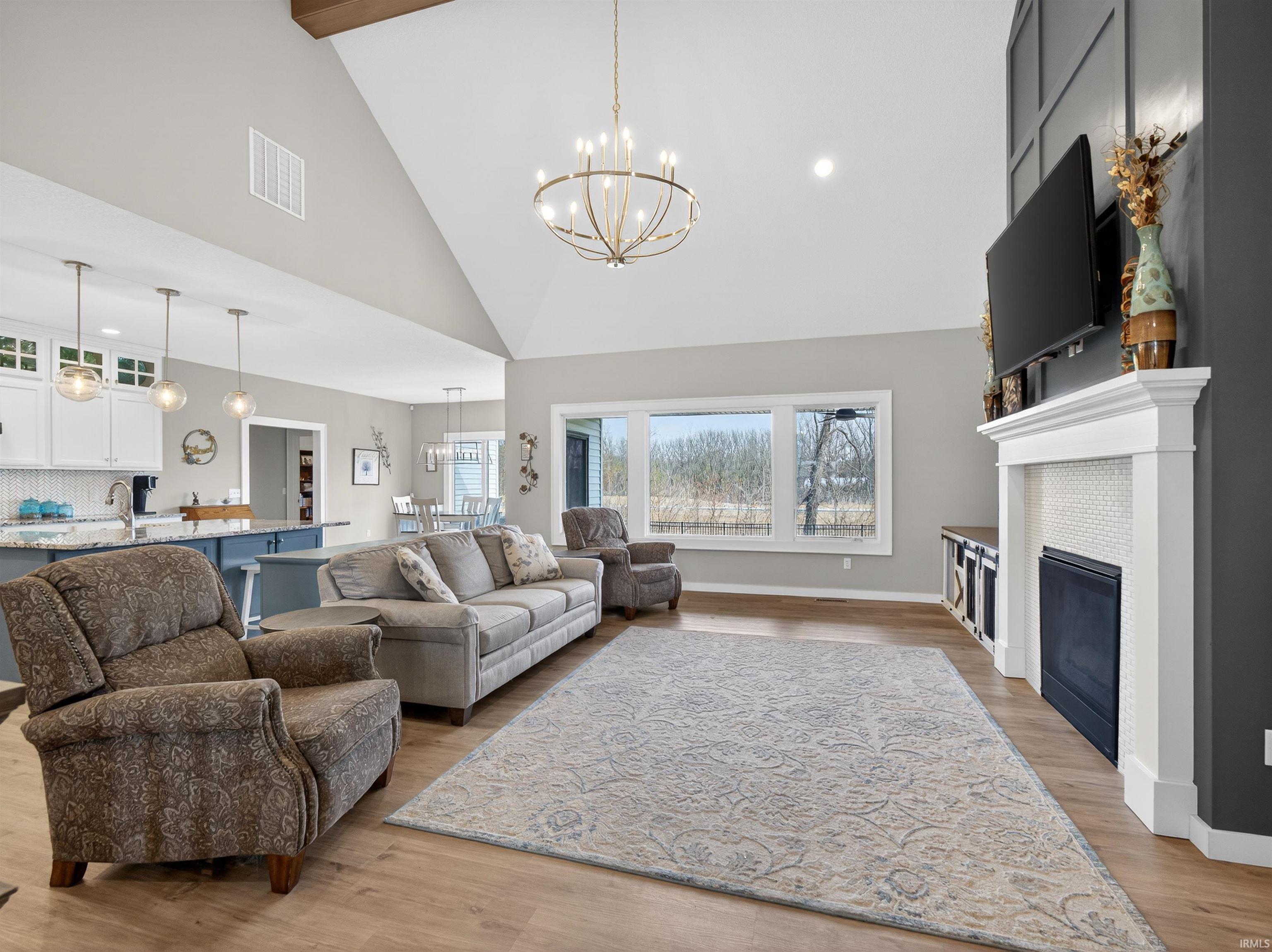 Living area with light wood-style floors, suspended lighting, lofted ceiling, and a fireplace