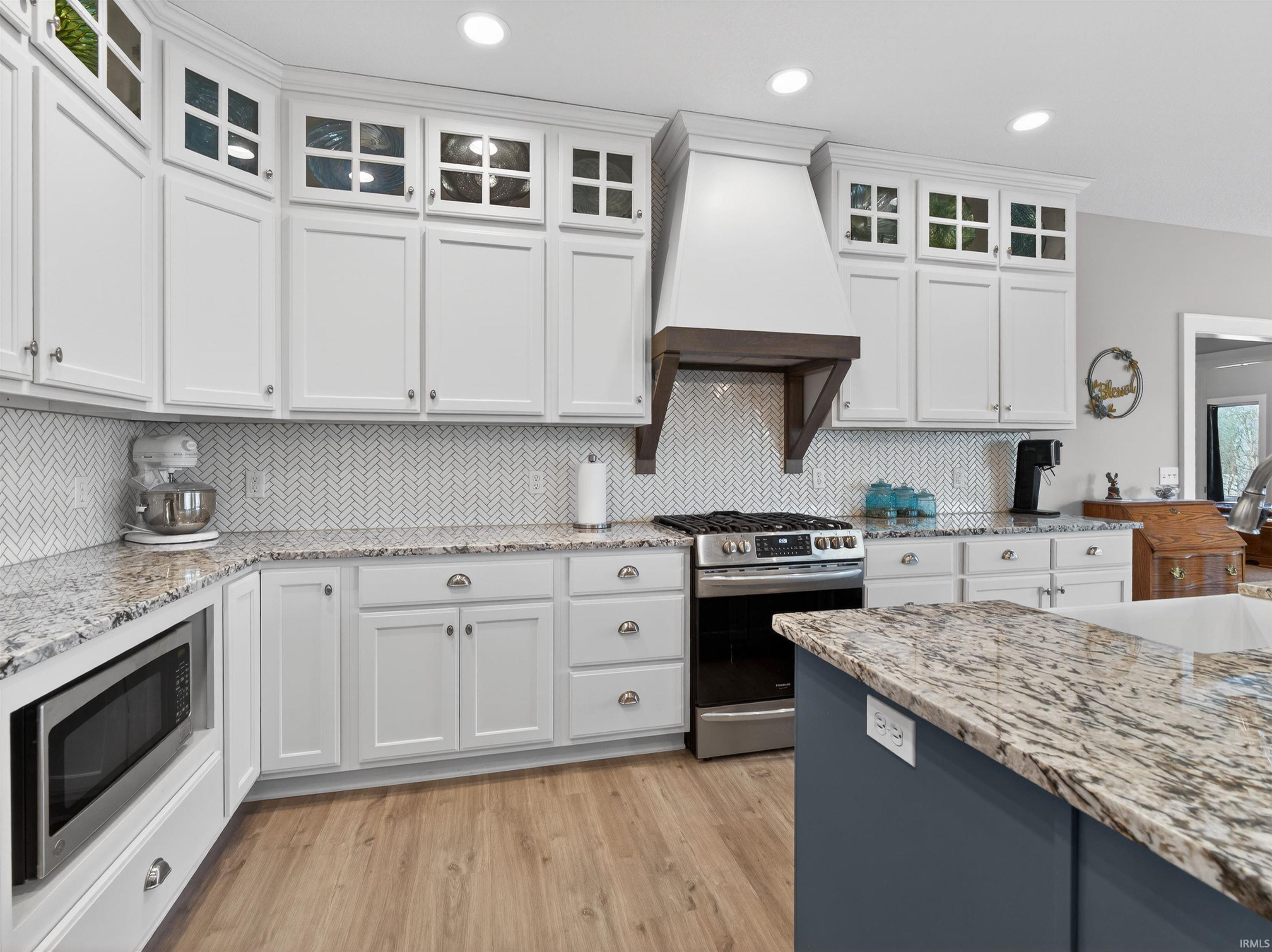 Dual tone kitchen featuring light stone counters, stainless steel appliances, light wood finished floors, glass fronted cabinets, and dual tone cabinets