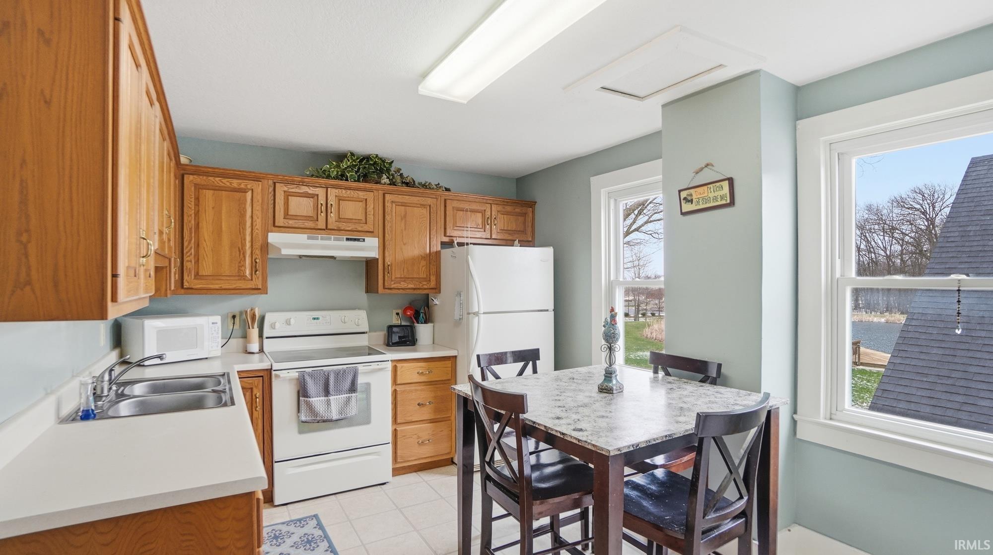 Kitchen featuring white appliances, light countertops, wood finish cabinetry, and light tile patterned flooring