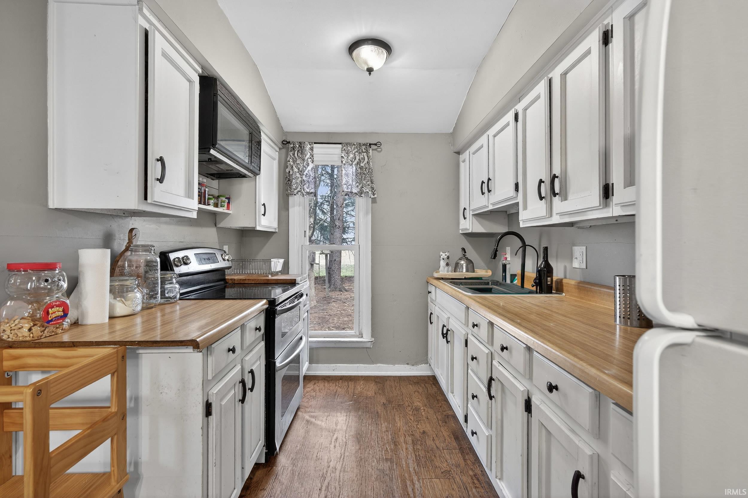 Kitchen with freestanding refrigerator, double oven range, black microwave, white cabinets, and light countertops