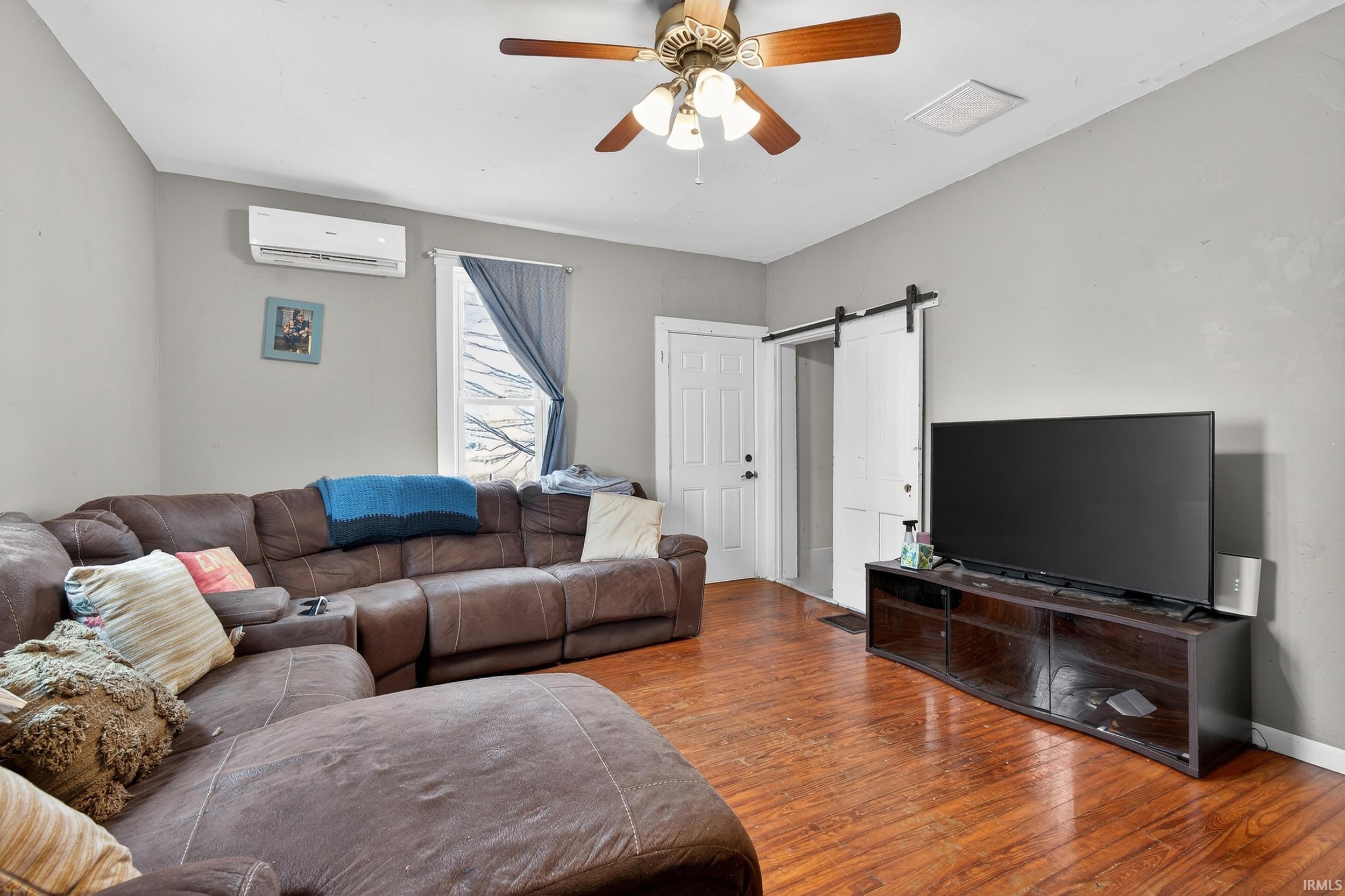 Living room with a barn door, ceiling fan, and wood-type flooring