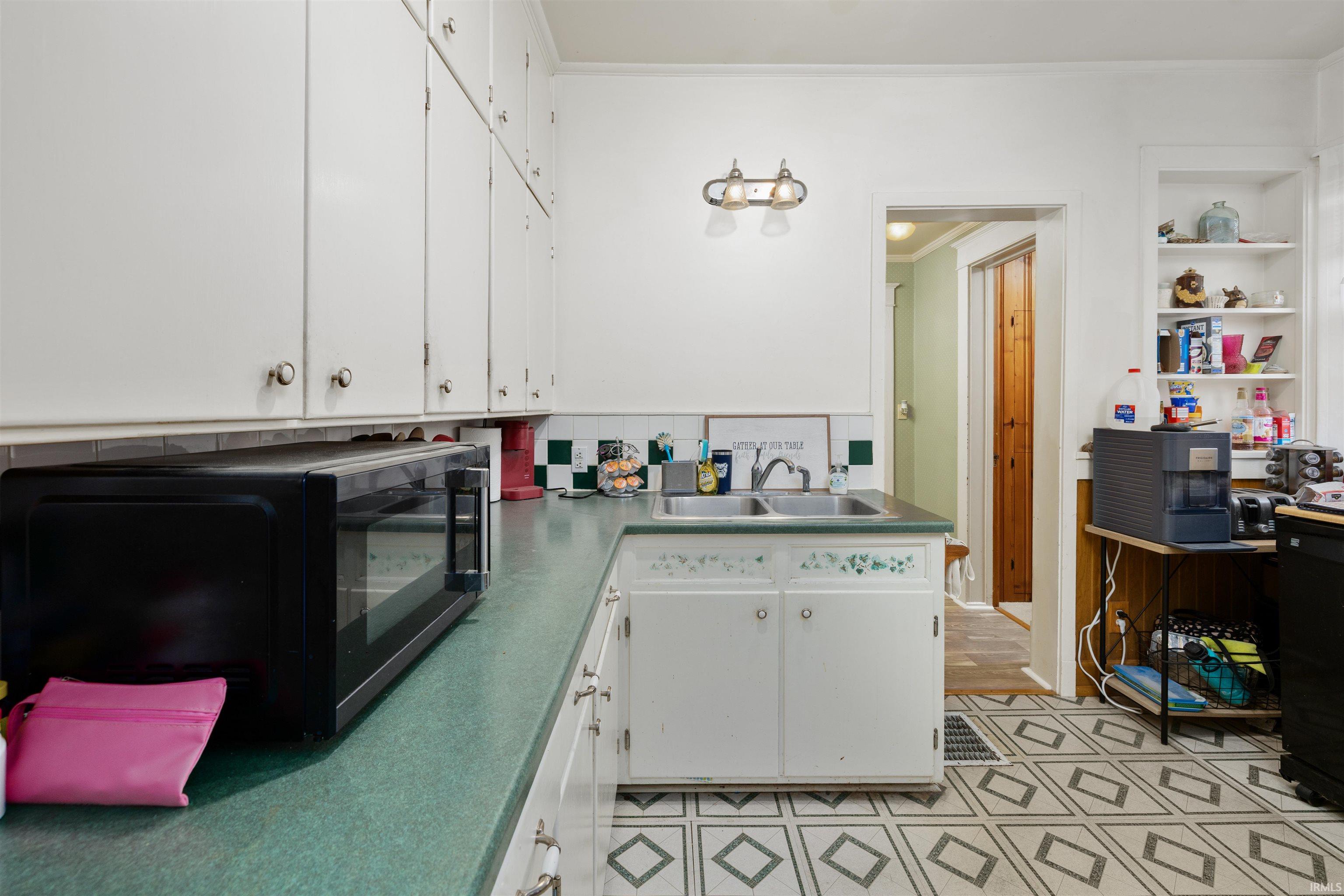 Kitchen featuring white cabinets, black microwave, crown molding, dark countertops, and backsplash