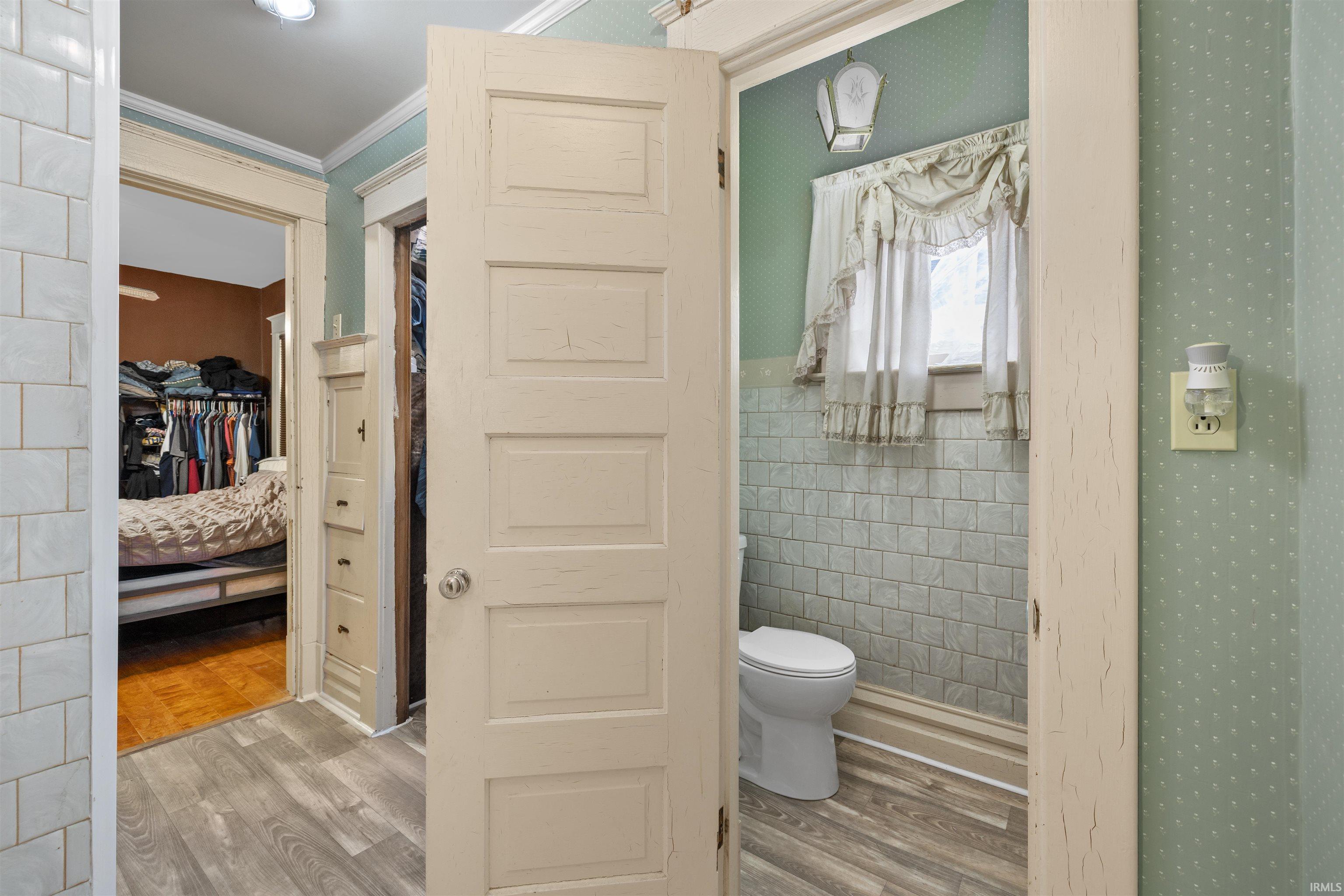 Bathroom with tile walls, light wood finished floors, ornamental molding, and a walk in closet