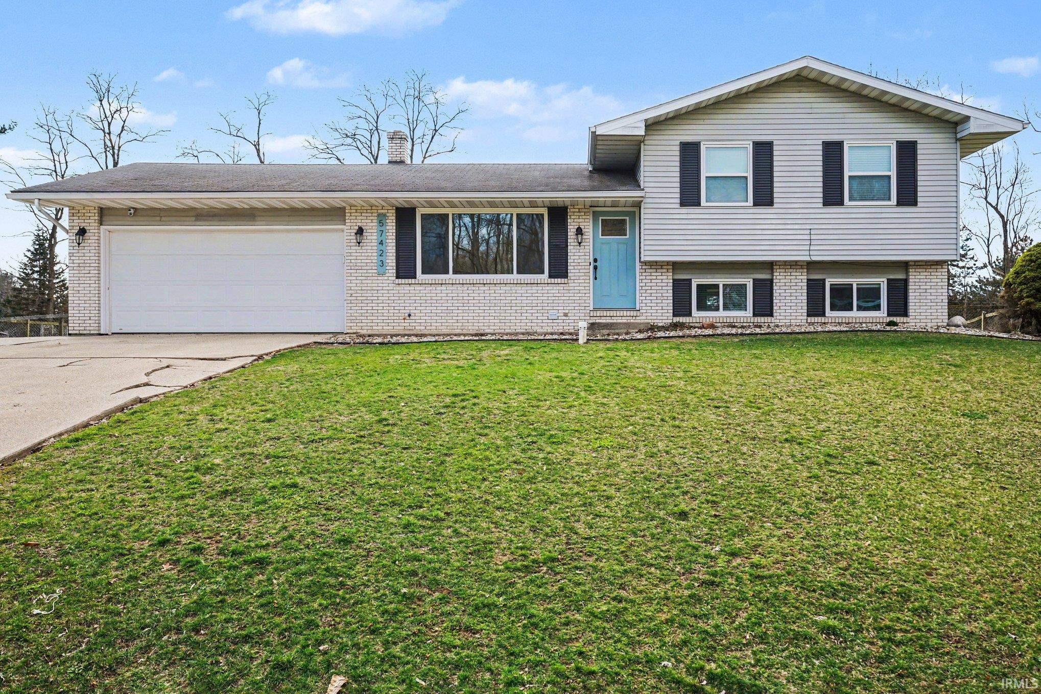Tri-level home with driveway, brick siding, a front yard, and a garage