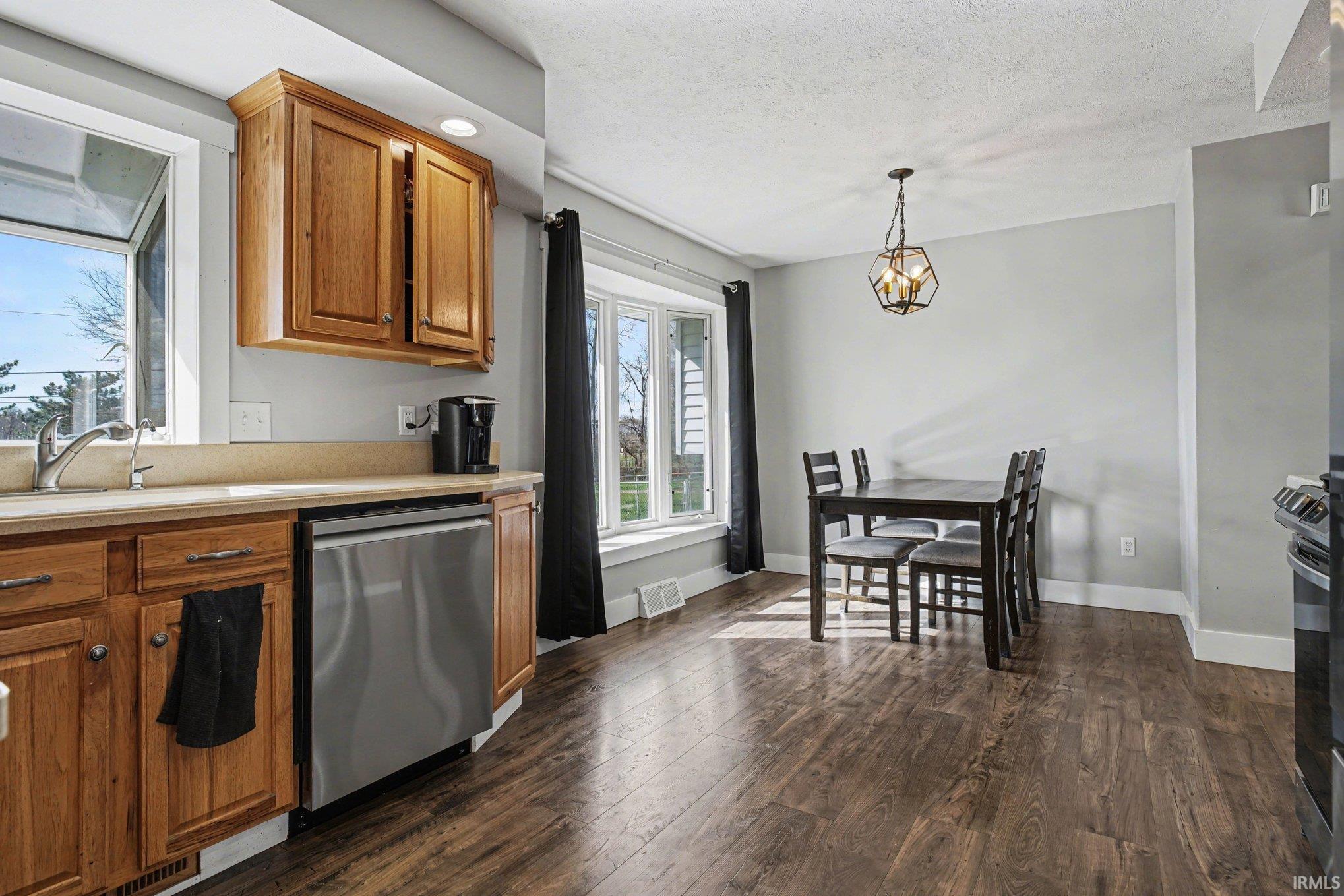Kitchen with light countertops, stainless steel appliances, wood finish cabinets, dark wood-style flooring, and pendant lighting