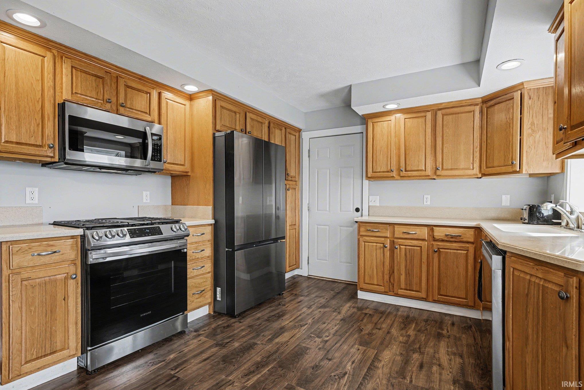 Kitchen featuring recessed lighting, stainless steel appliances, light countertops, dark wood-style flooring, and wood finish cabinetry