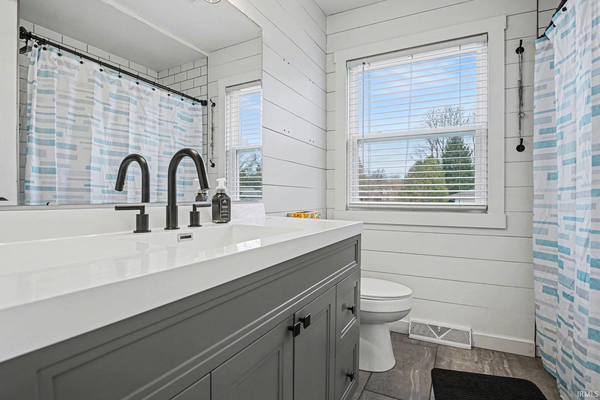 Full bathroom with wooden walls, vanity, a shower with shower curtain, and healthy amount of natural light