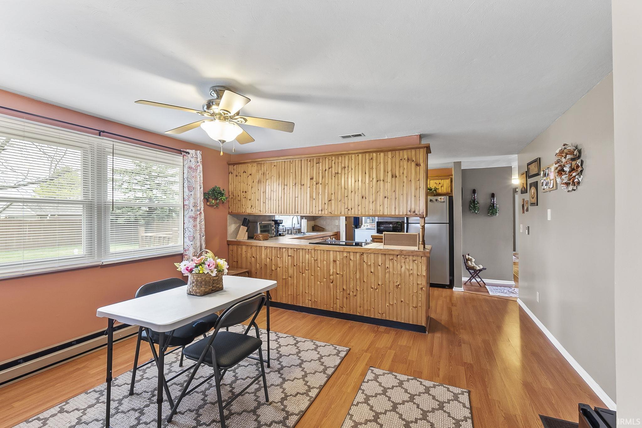 Kitchen with freestanding refrigerator, a peninsula, light wood-type flooring, a ceiling fan, and baseboard heating