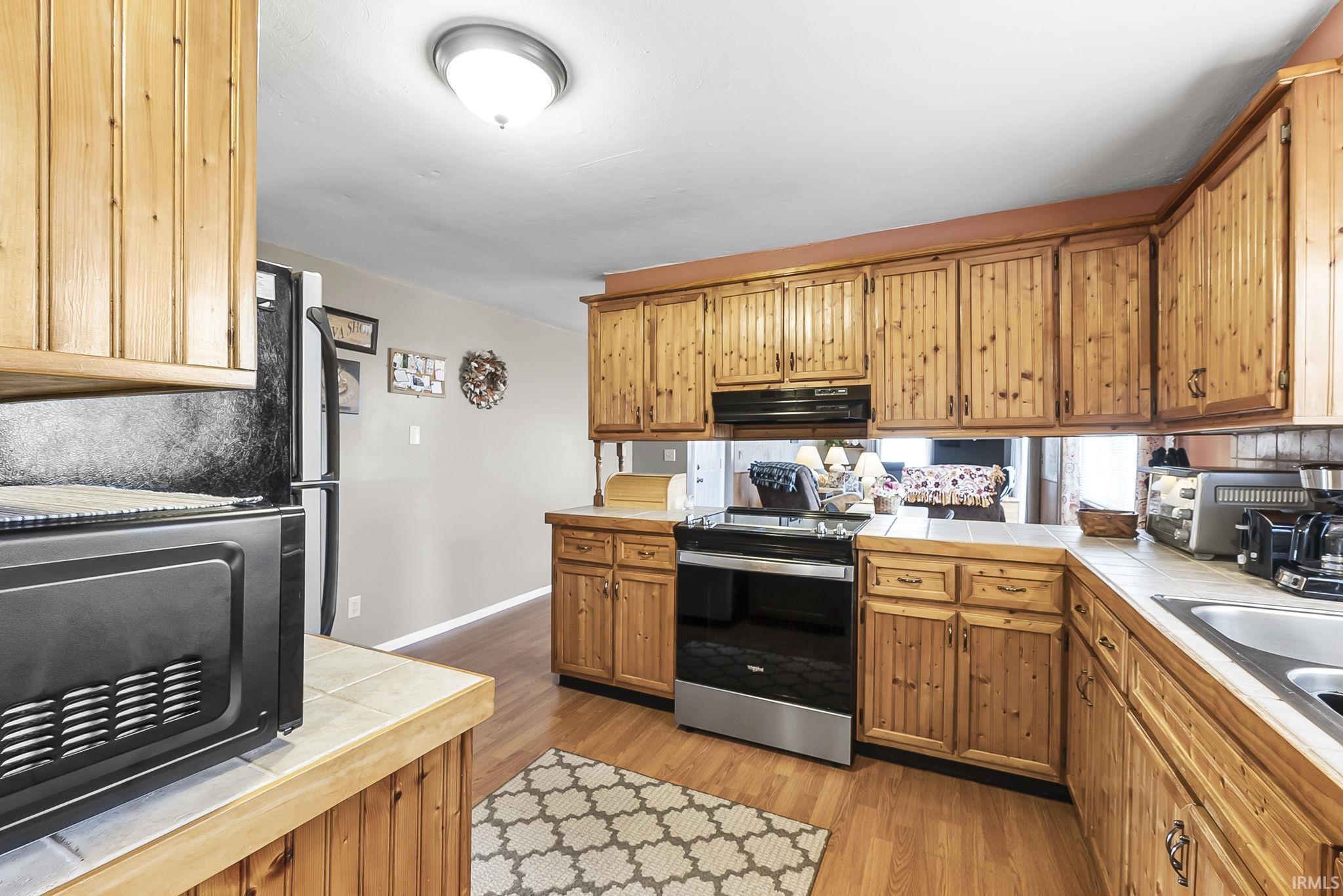 Kitchen featuring stainless steel appliances, wood finish cabinets, light wood-style floors, and tile countertops
