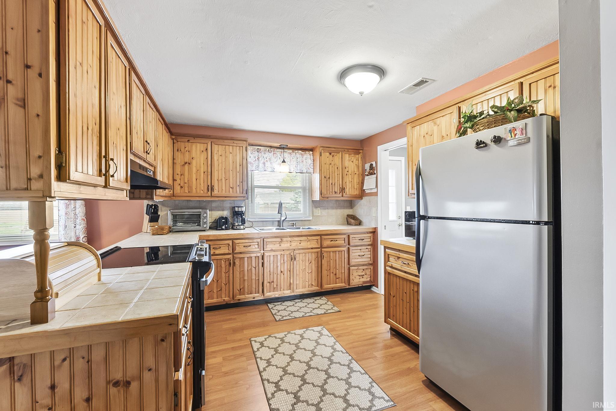 Kitchen featuring tile countertops, stainless steel appliances, light wood finished floors, and tasteful backsplash