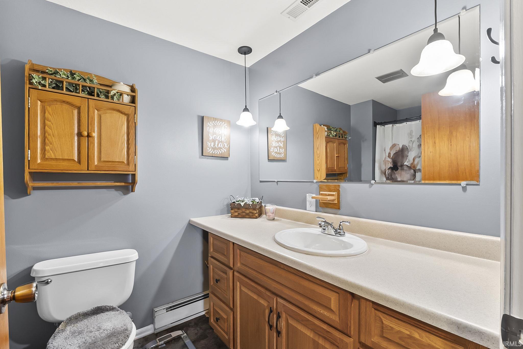 Bathroom featuring a shower with curtain, a baseboard heating unit, and vanity