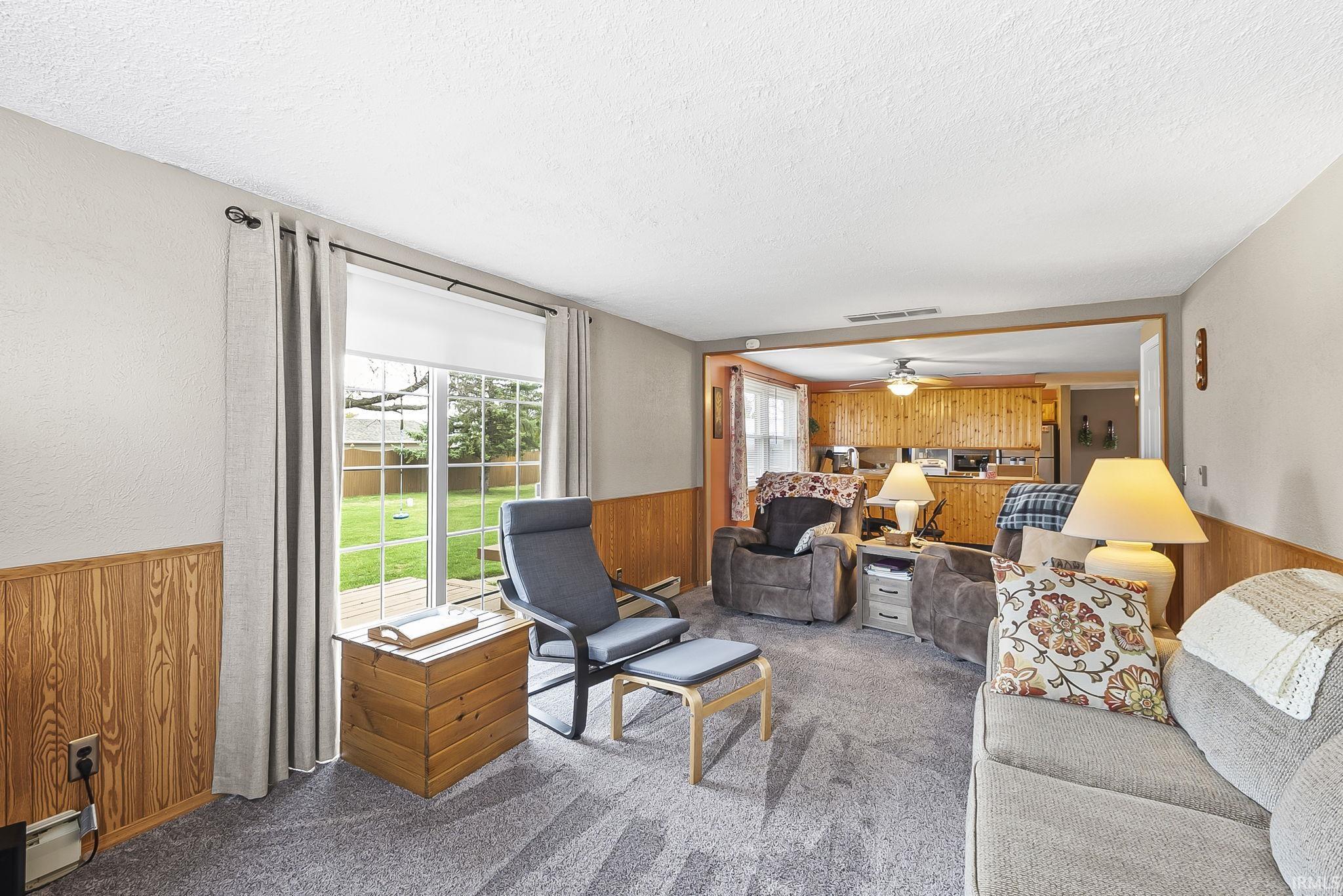 Carpeted living room with wood walls, wainscoting, ceiling fan, and a textured ceiling