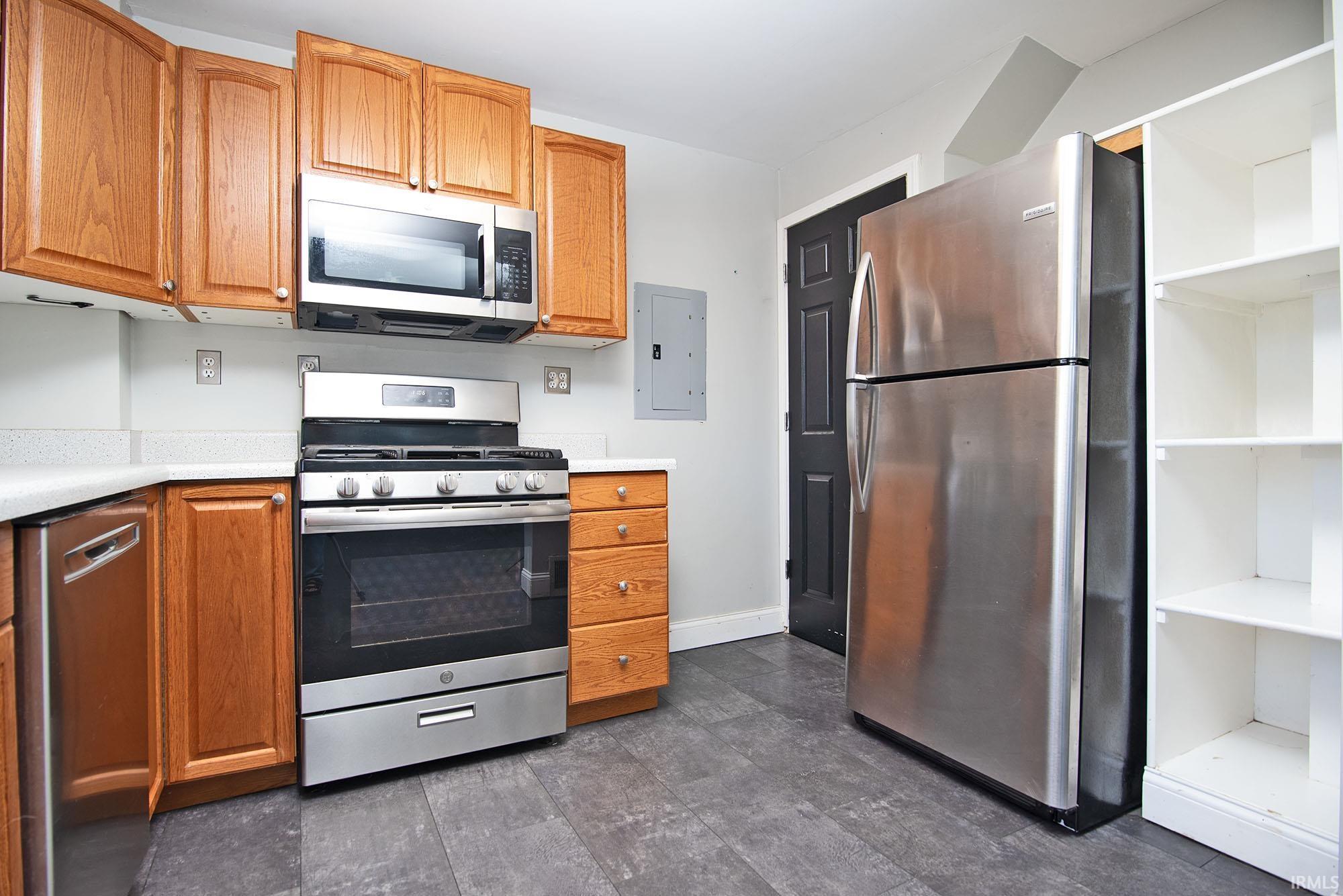 Kitchen with stainless steel appliances, light countertops, electric panel, and wood finish cabinetry