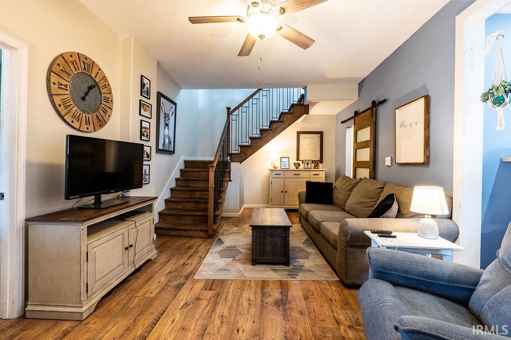 Living area with a barn door, light wood-style flooring, and ceiling fan