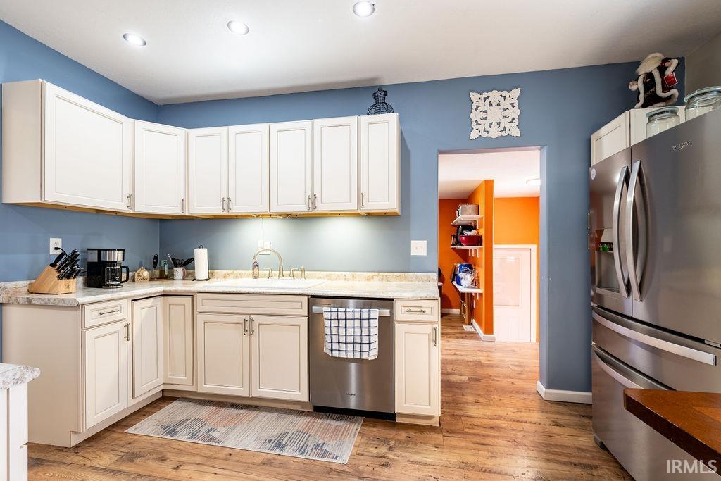 Kitchen featuring stainless steel appliances, light wood-type flooring, light stone countertops, and white cabinets