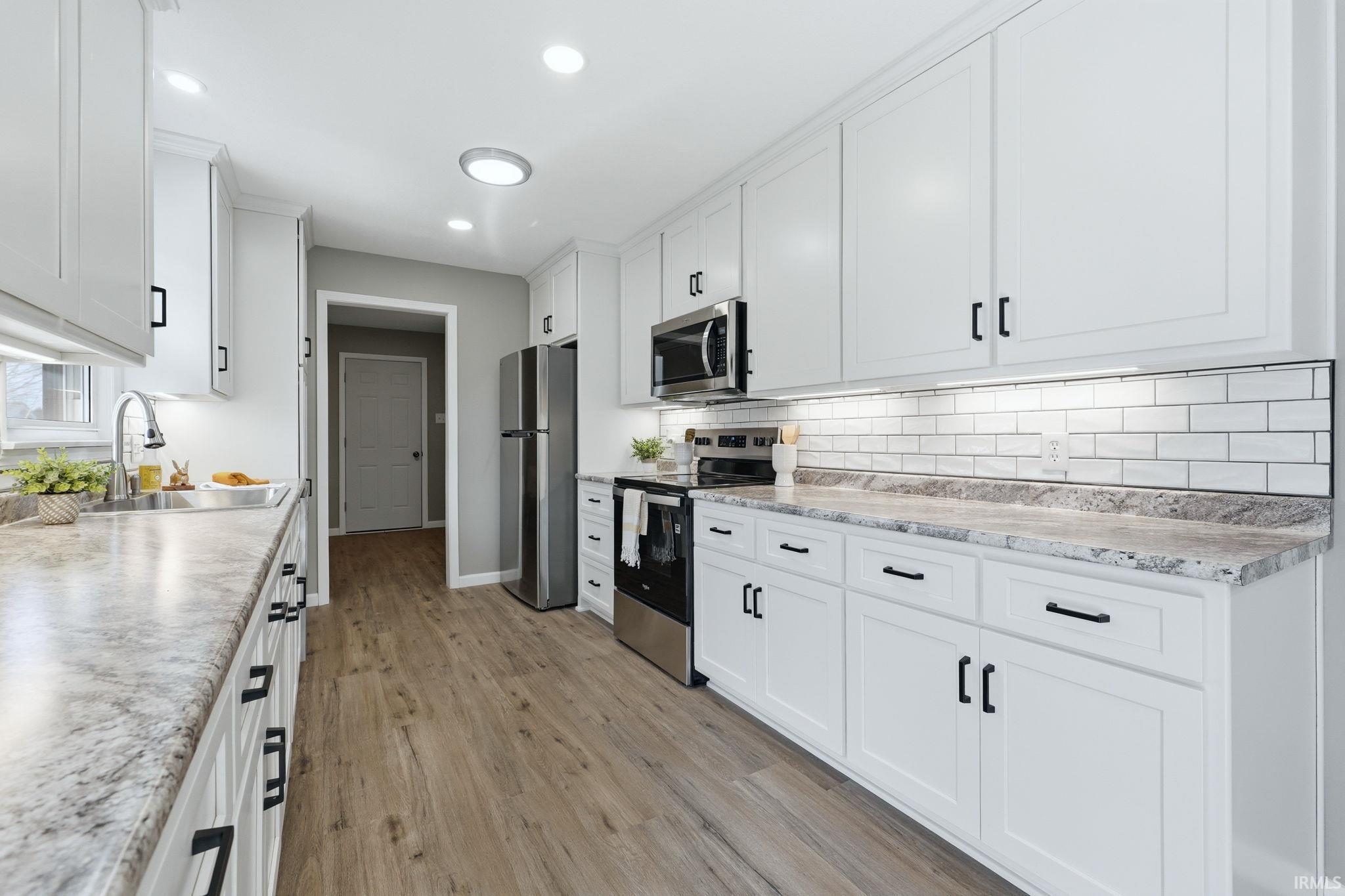 Kitchen with stainless steel appliances, light countertops, white cabinets, light wood-type flooring, and recessed lighting