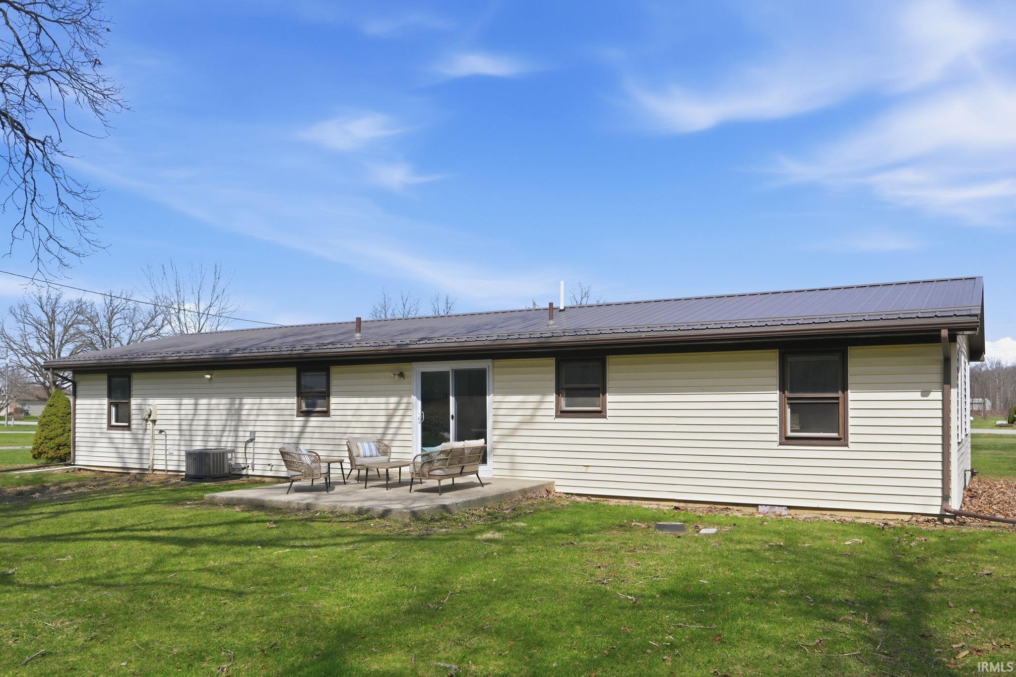 Rear view of property featuring a lawn, a patio area, and a metal roof