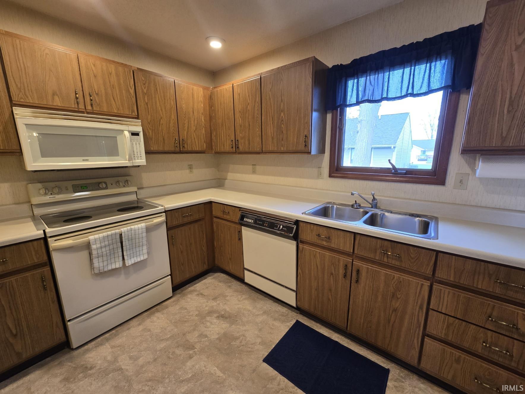 Kitchen with white appliances, light countertops, and wood finish cabinetry