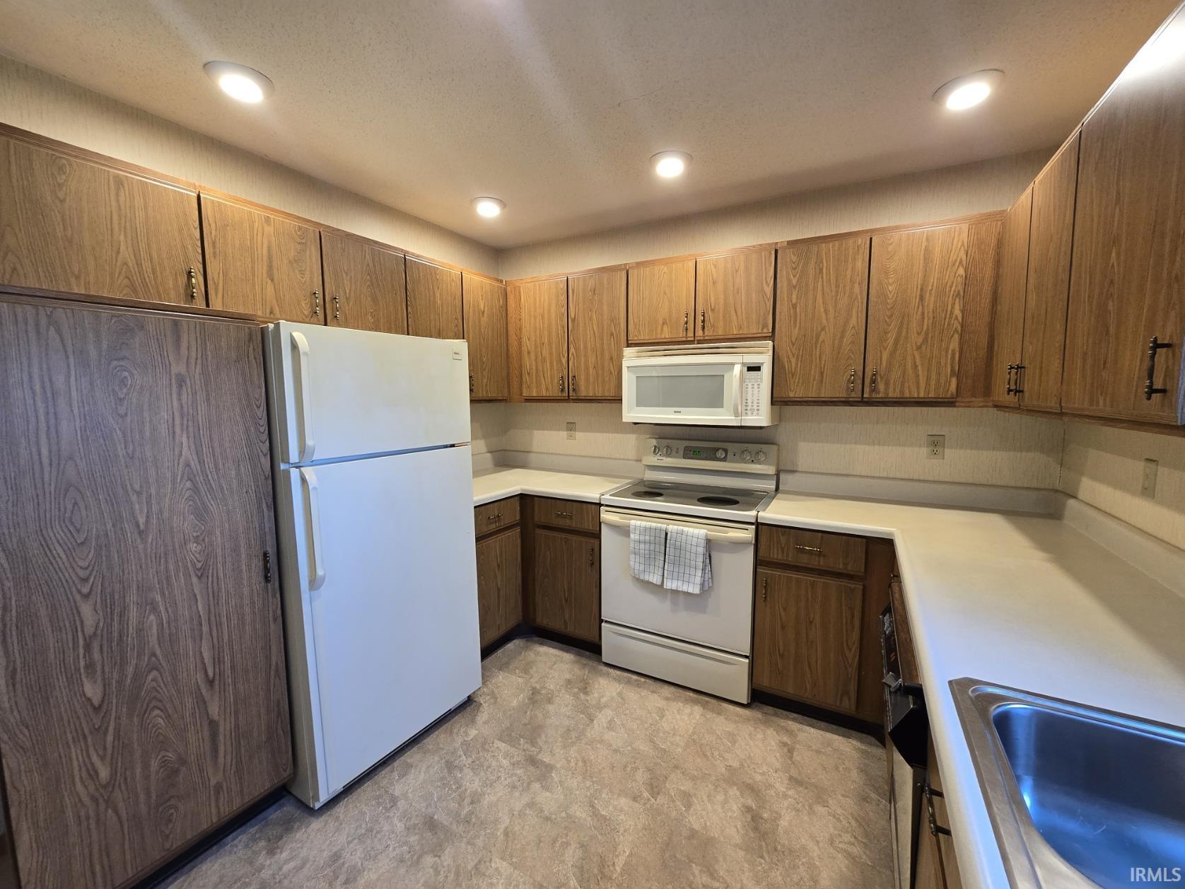 Kitchen featuring white appliances, light countertops, recessed lighting, wood finish cabinetry, and a textured ceiling