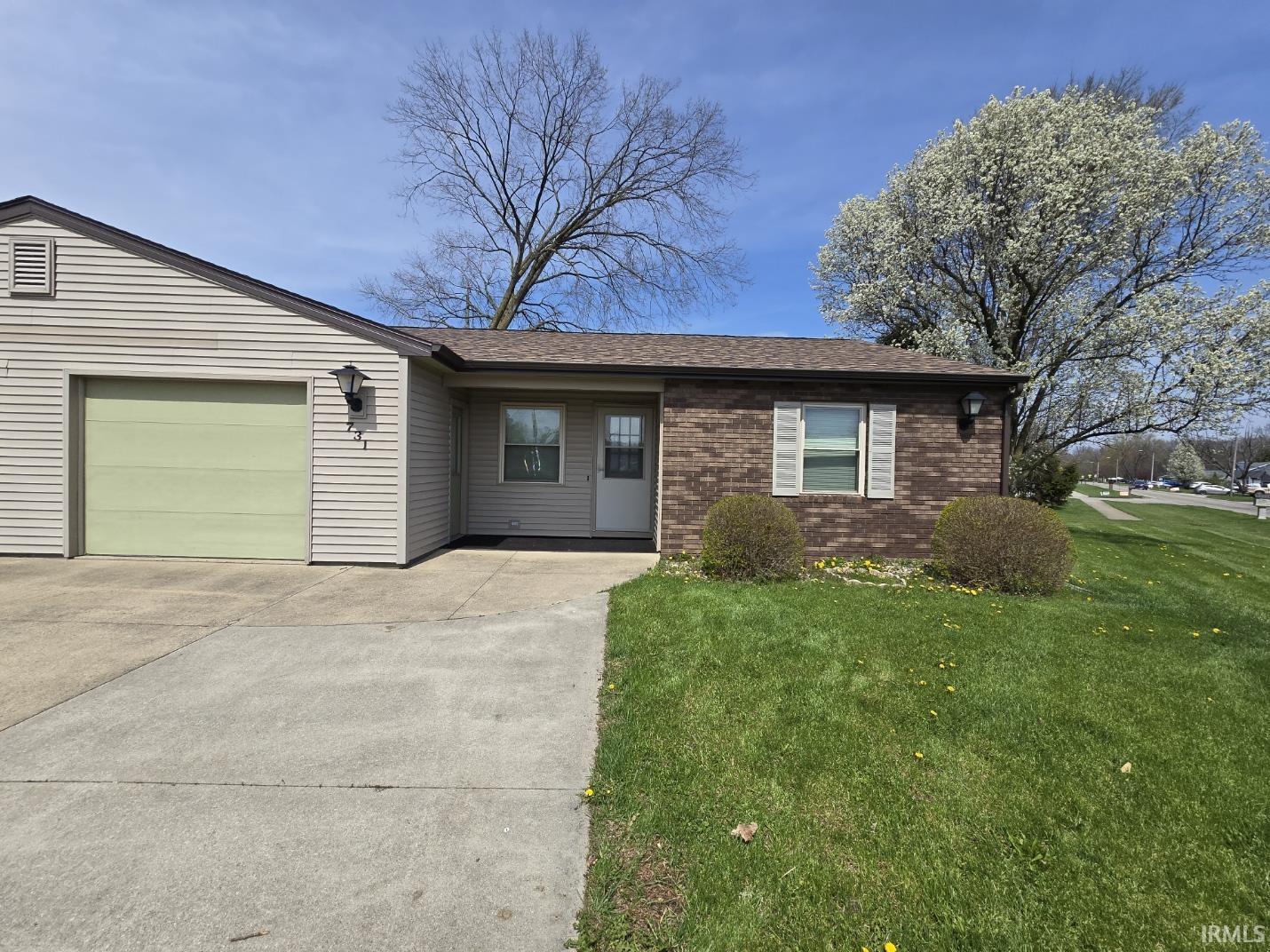 Ranch-style home with brick siding, an attached garage, driveway, a front lawn, and a shingled roof