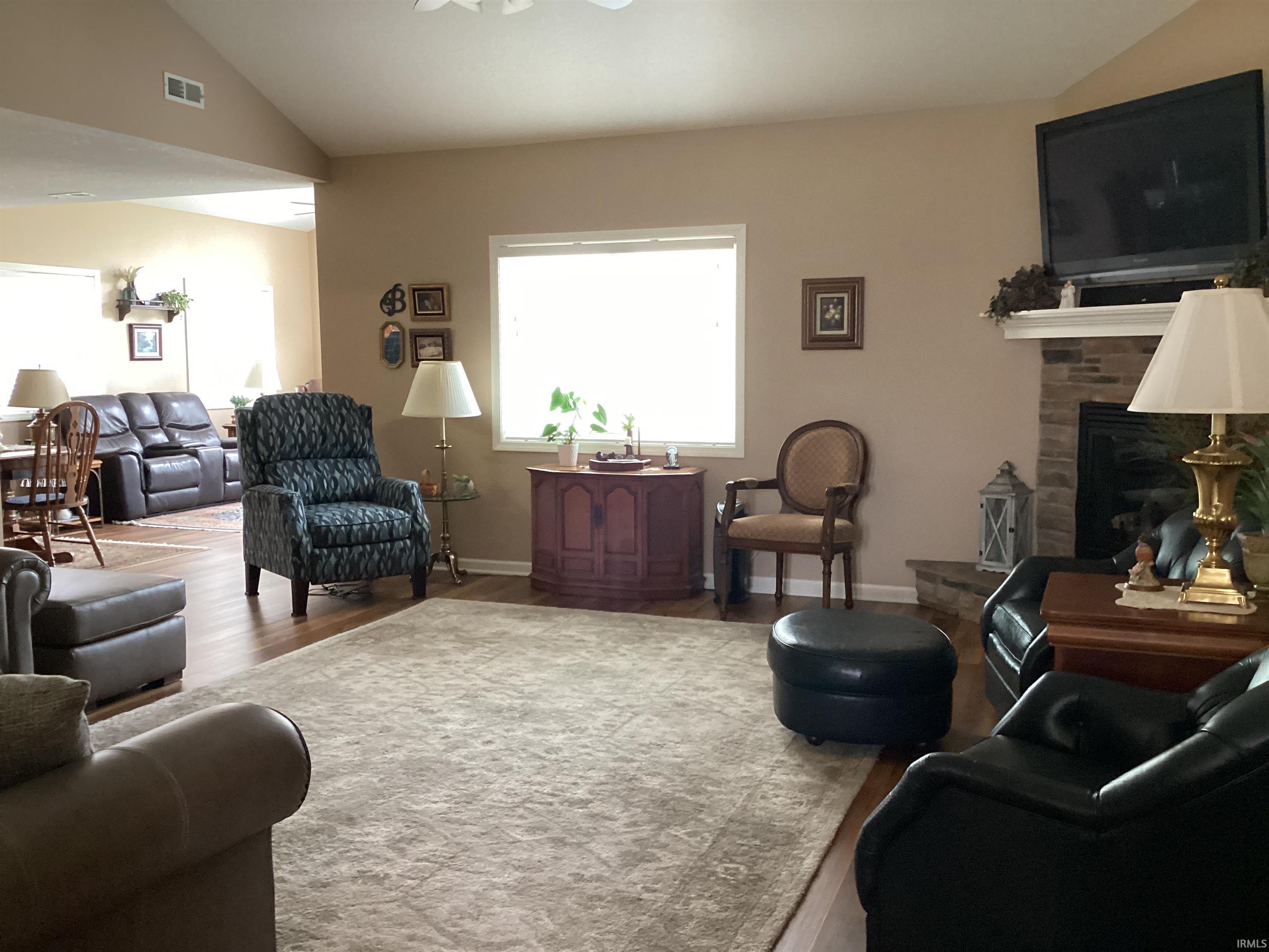 Living room with vaulted ceiling, wood finished floors, a fireplace, and a ceiling fan