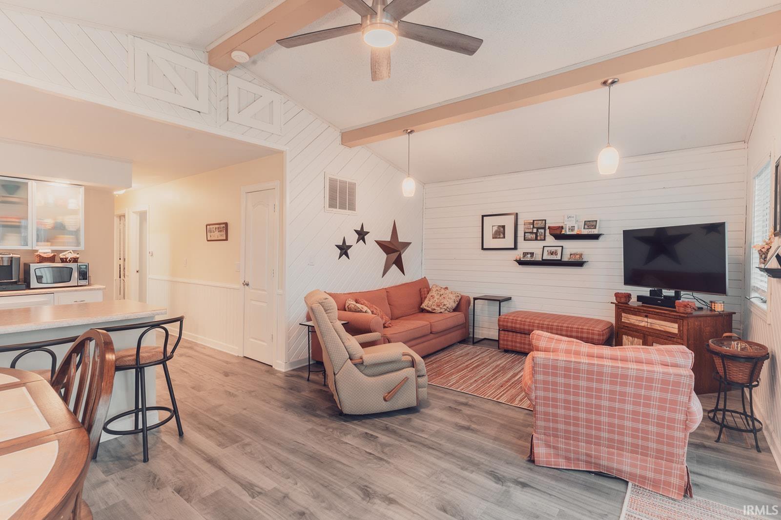 Living room featuring beam ceiling, wood walls, light wood-type flooring, and ceiling fan