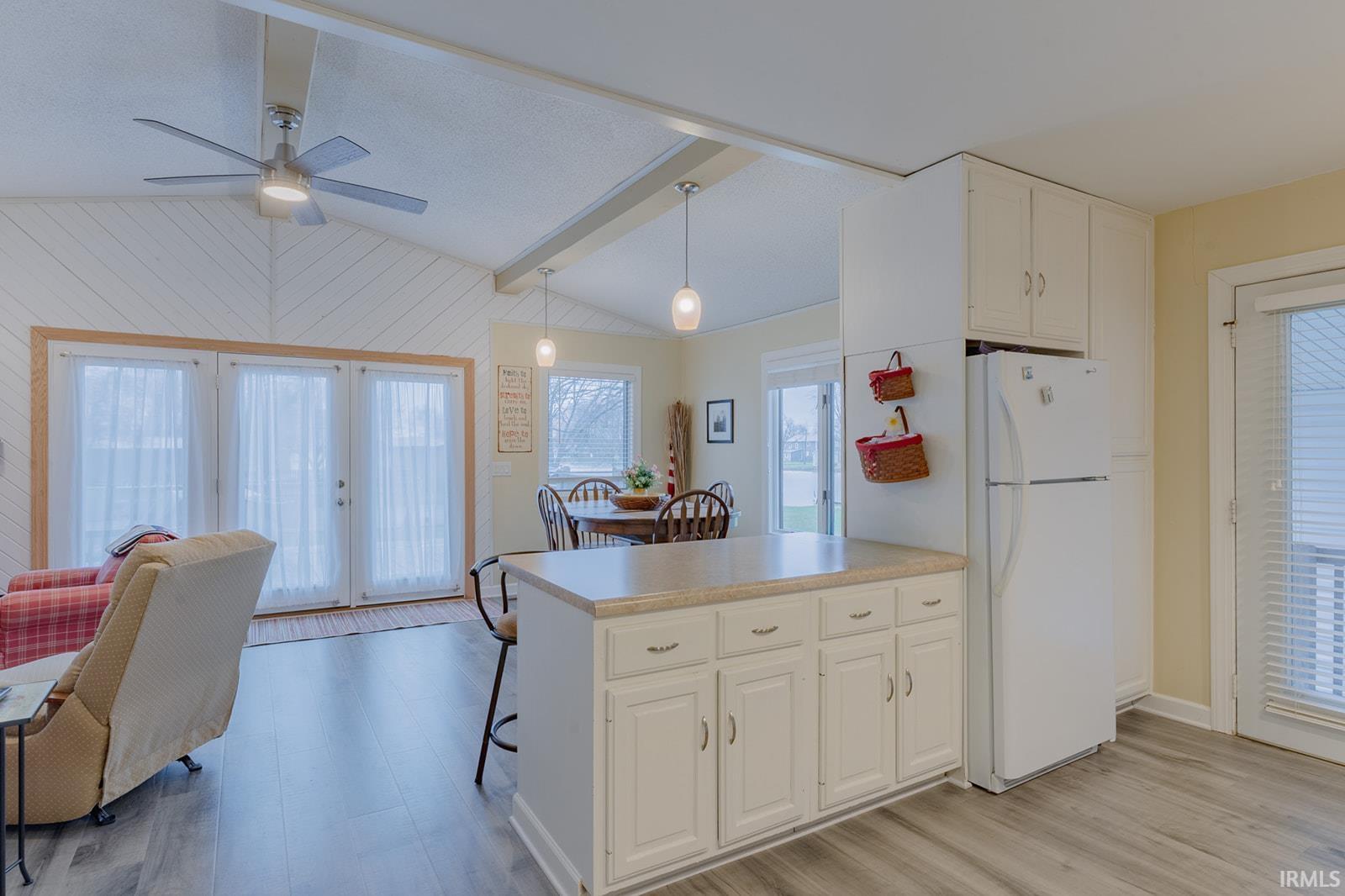 Kitchen with freestanding refrigerator, a peninsula, light countertops, white cabinets, and light wood-type flooring
