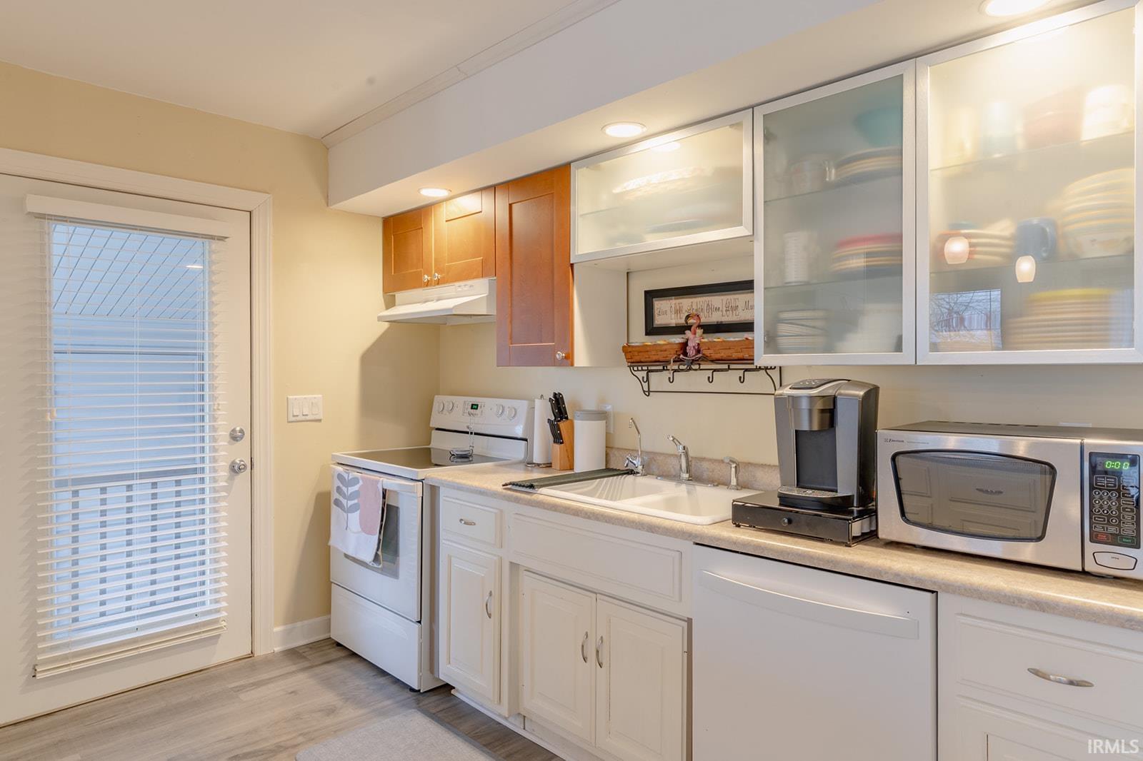 Kitchen featuring white appliances, light countertops, glass insert cabinets, recessed lighting, and light wood-type flooring
