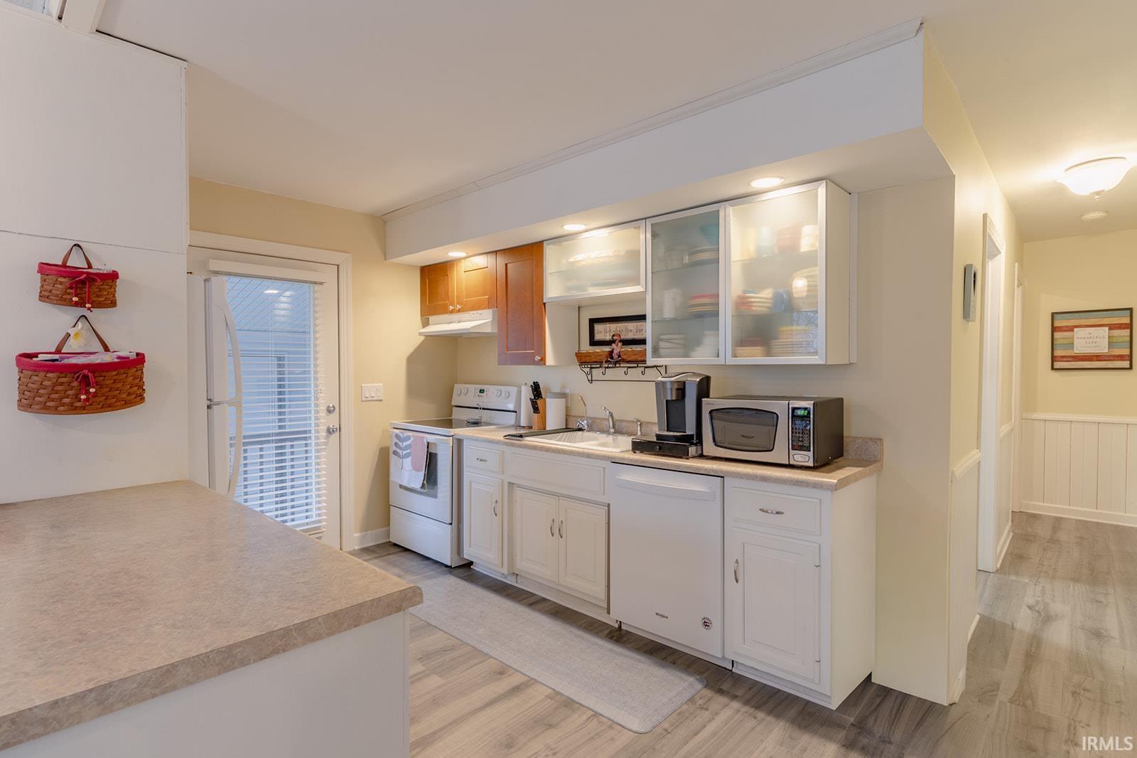 Kitchen with white appliances, light wood finished floors, glass fronted cabinets, light countertops, and white cabinets