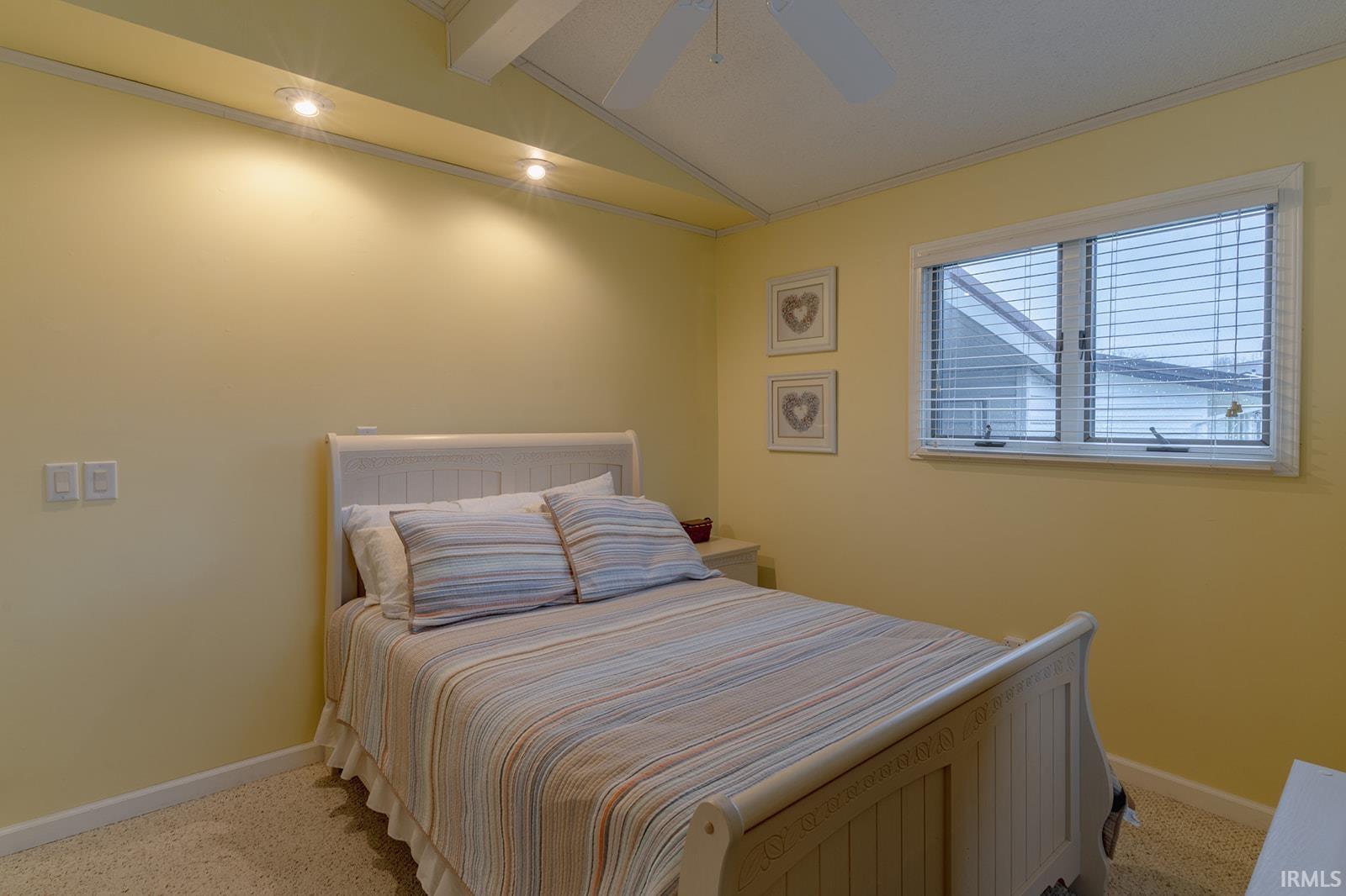 Bedroom featuring lofted ceiling with beams, light colored carpet, crown molding, and a ceiling fan
