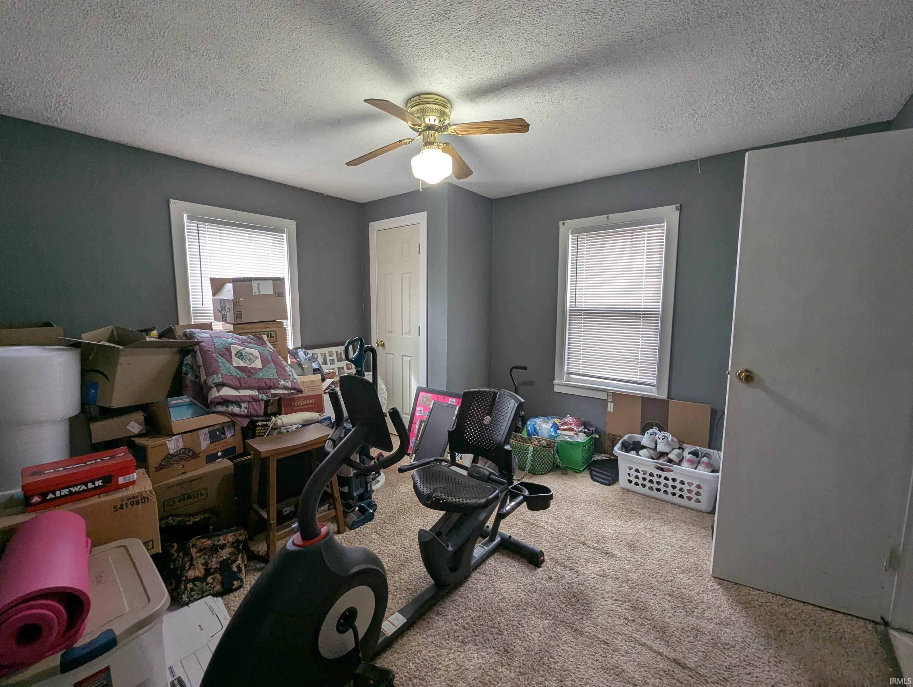 Exercise room with carpet, ceiling fan, and a textured ceiling