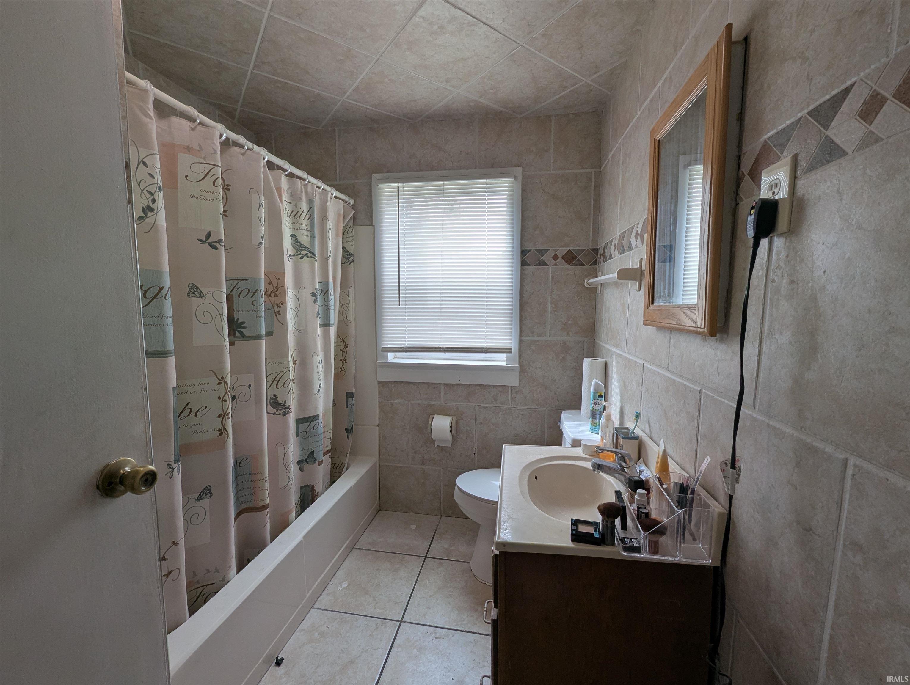 Bathroom featuring vanity, shower / bath combination with curtain, tile walls, light tile patterned flooring, and plenty of natural light