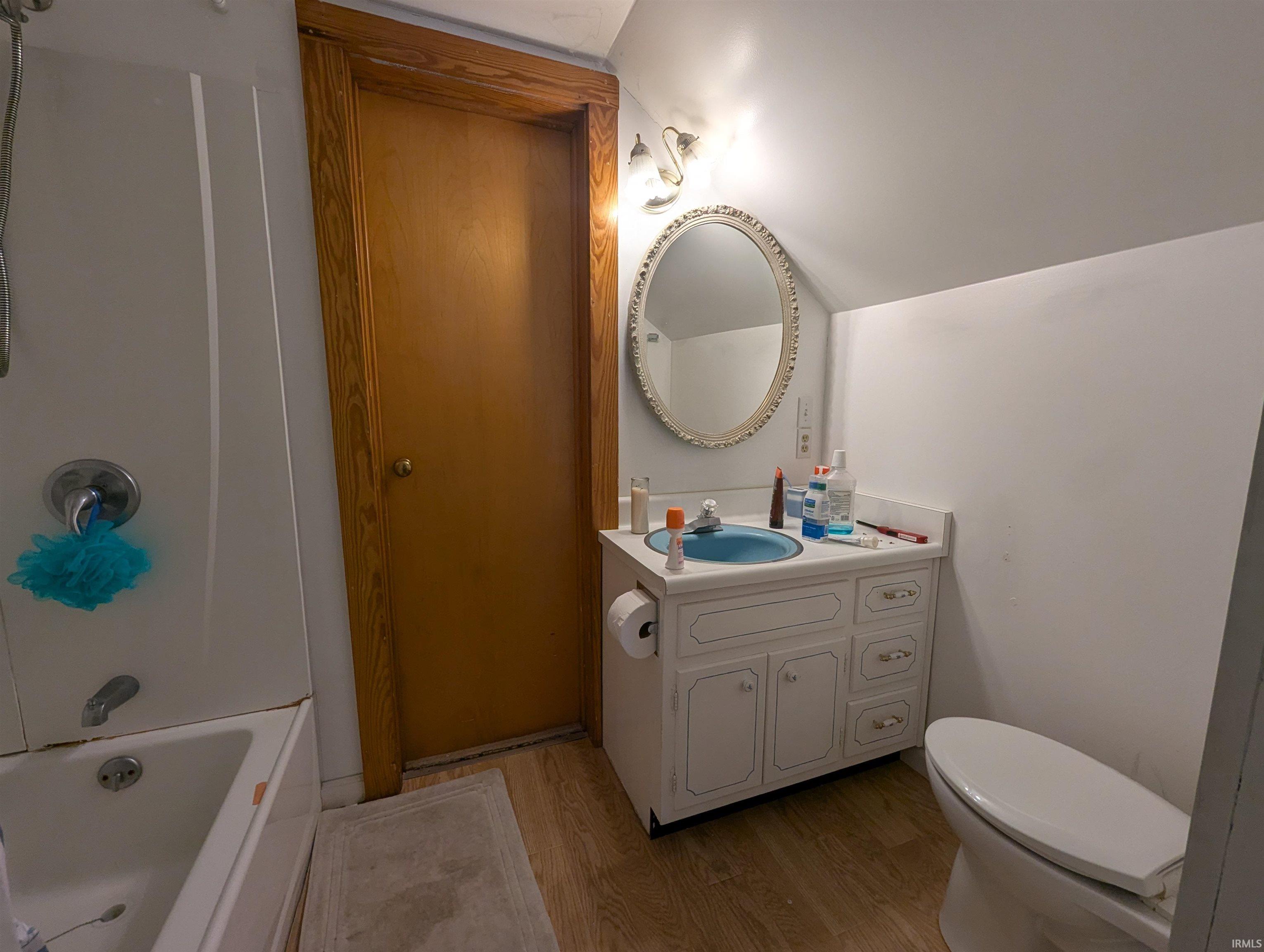 Bathroom featuring light wood-style flooring, vanity, vaulted ceiling, and bathing tub / shower combination