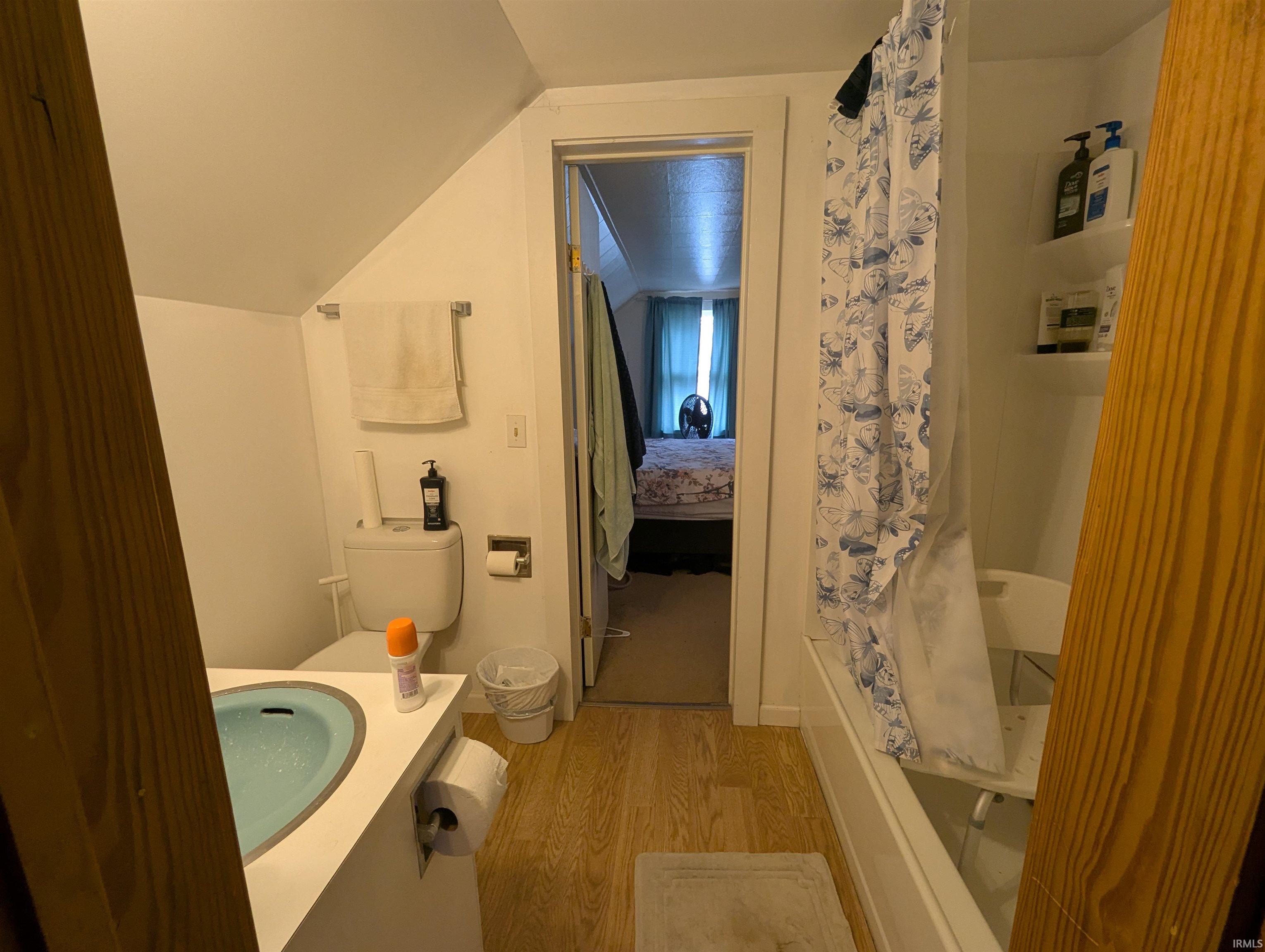 Ensuite bathroom with vanity, light wood-type flooring, shower / bath combo, and lofted ceiling