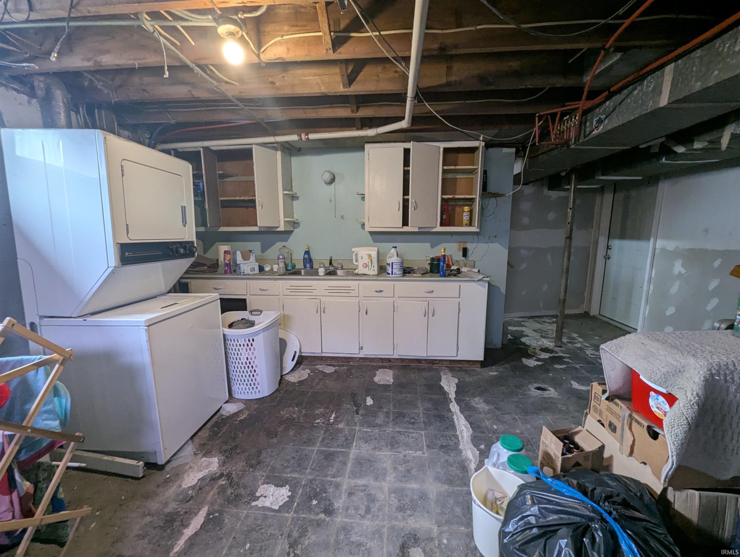 Unfinished below grade area featuring stacked washer and clothes dryer and a sink