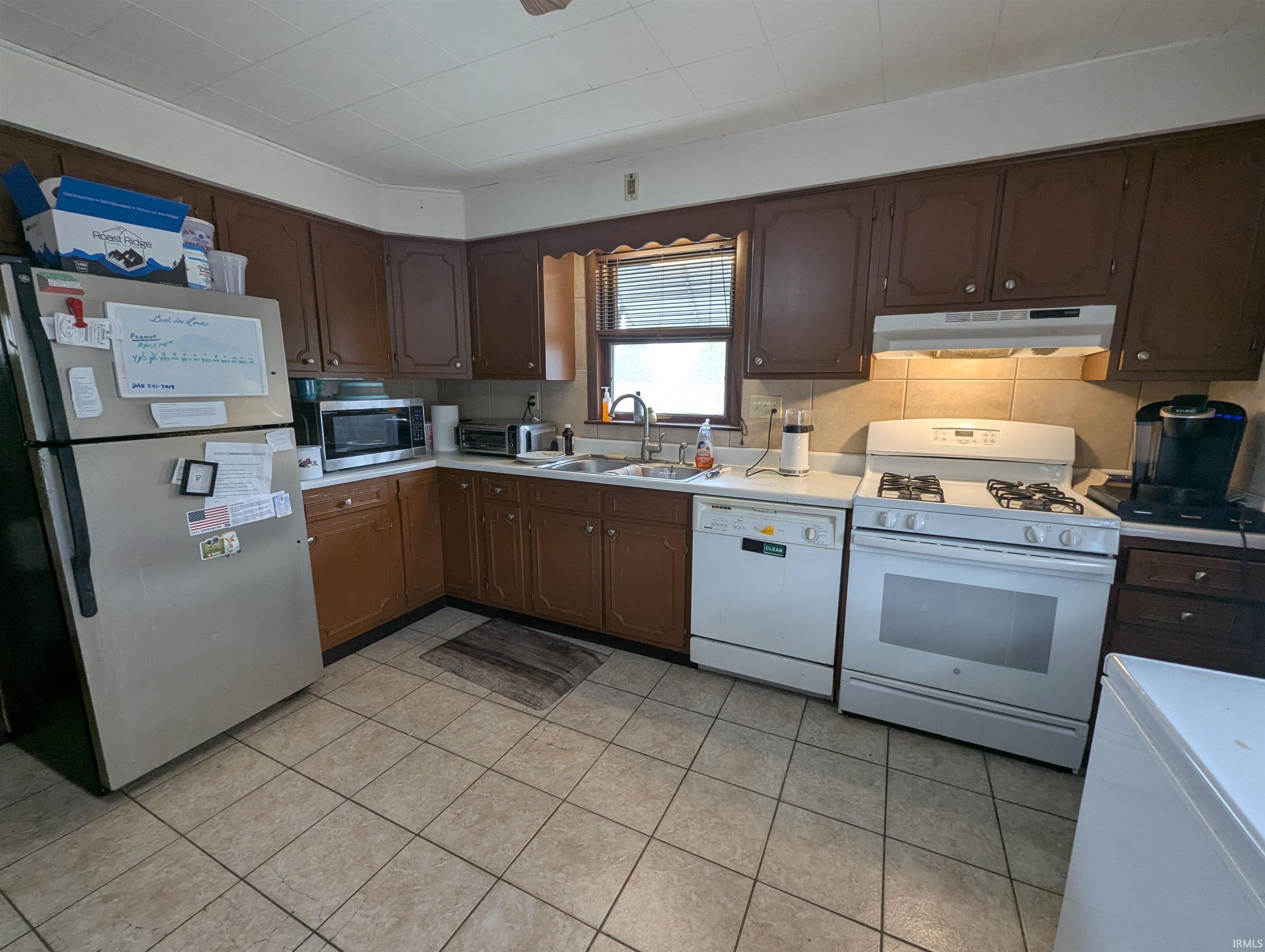 Kitchen featuring stainless steel appliances, dark wood finish cabinetry, light countertops, and light tile patterned floors