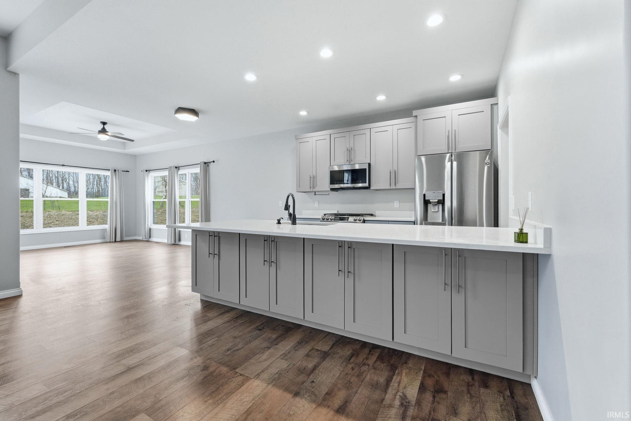 Open-concept kitchen featuring an island with a white countertop, grey shaker-style cabinetry, stainless steel appliances, and wood-finish flooring