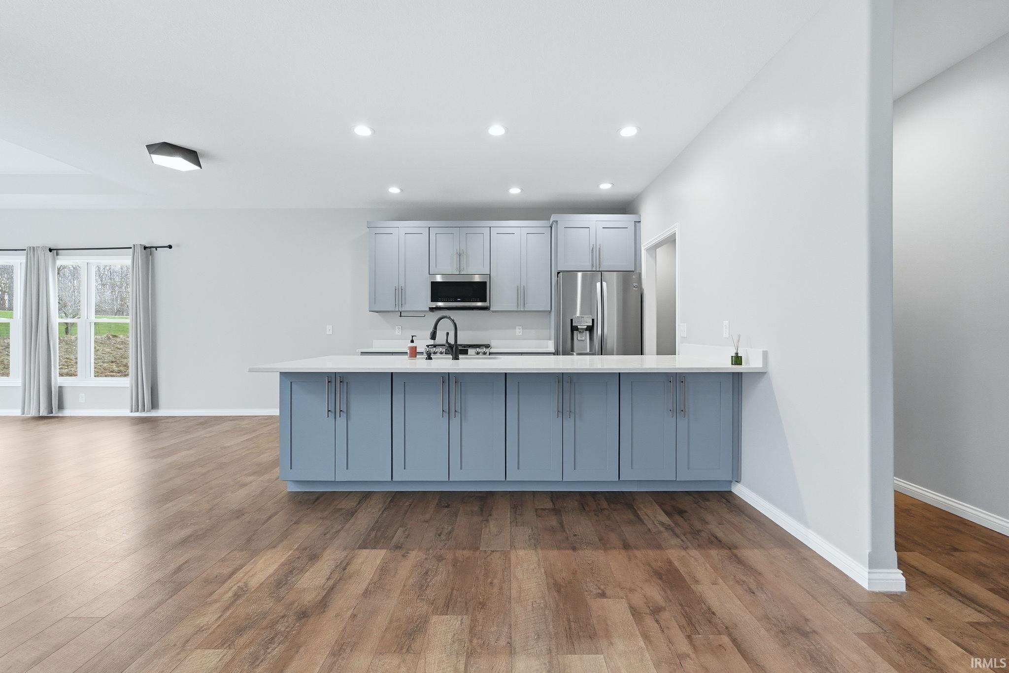 Kitchen featuring a peninsula, stainless steel appliances, recessed lighting, light wood finished floors, and light stone countertops