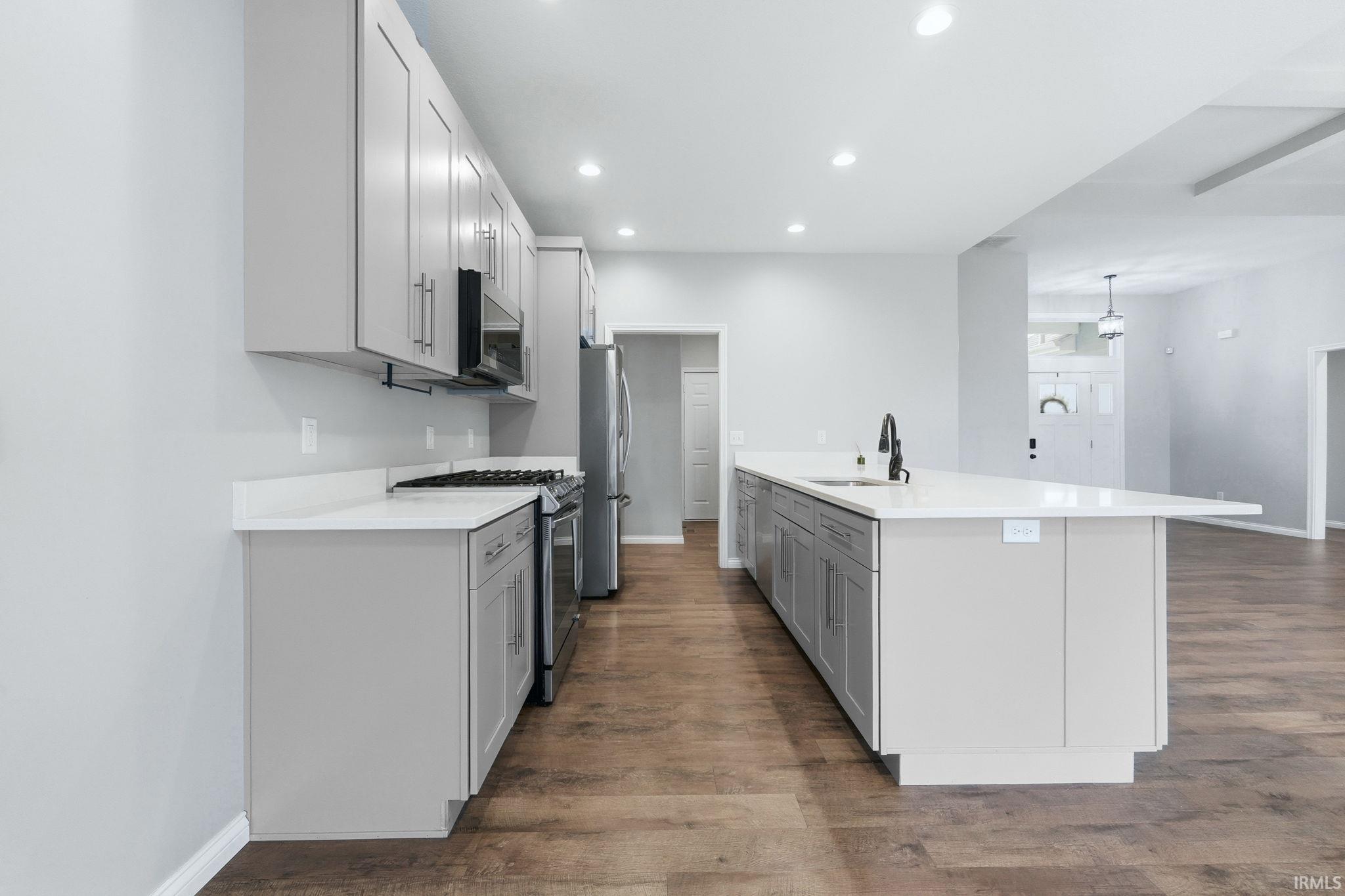Contemporary kitchen featuring light gray cabinetry, white countertops, stainless steel appliances, and wood-finish flooring