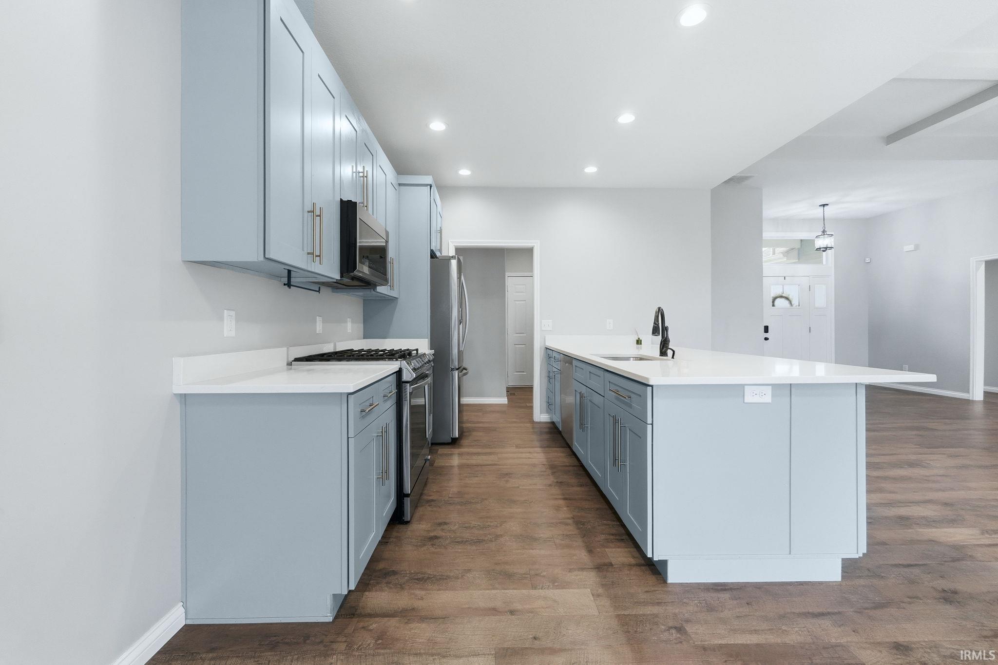 Kitchen featuring stainless steel appliances, dark wood-style flooring, a kitchen island with sink, and light stone countertops