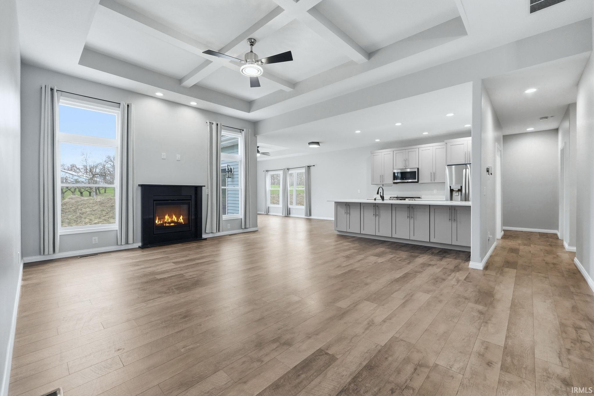 Spacious open-concept living area featuring wood-finish flooring, a contemporary fireplace with a black mantel, and large windows
